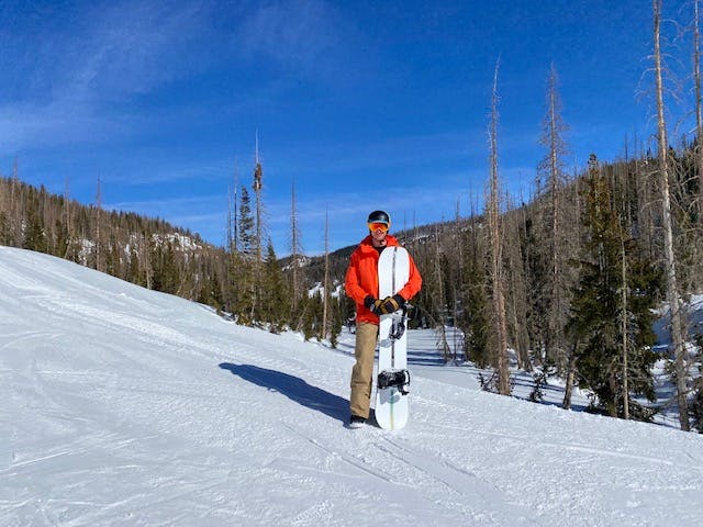 A man standing with the Burton Malavita Snowboard Bindings mounted to a snowboard.