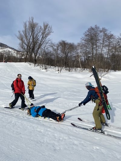 Four skiers. One is laying on hie back and the others are trying to help him.