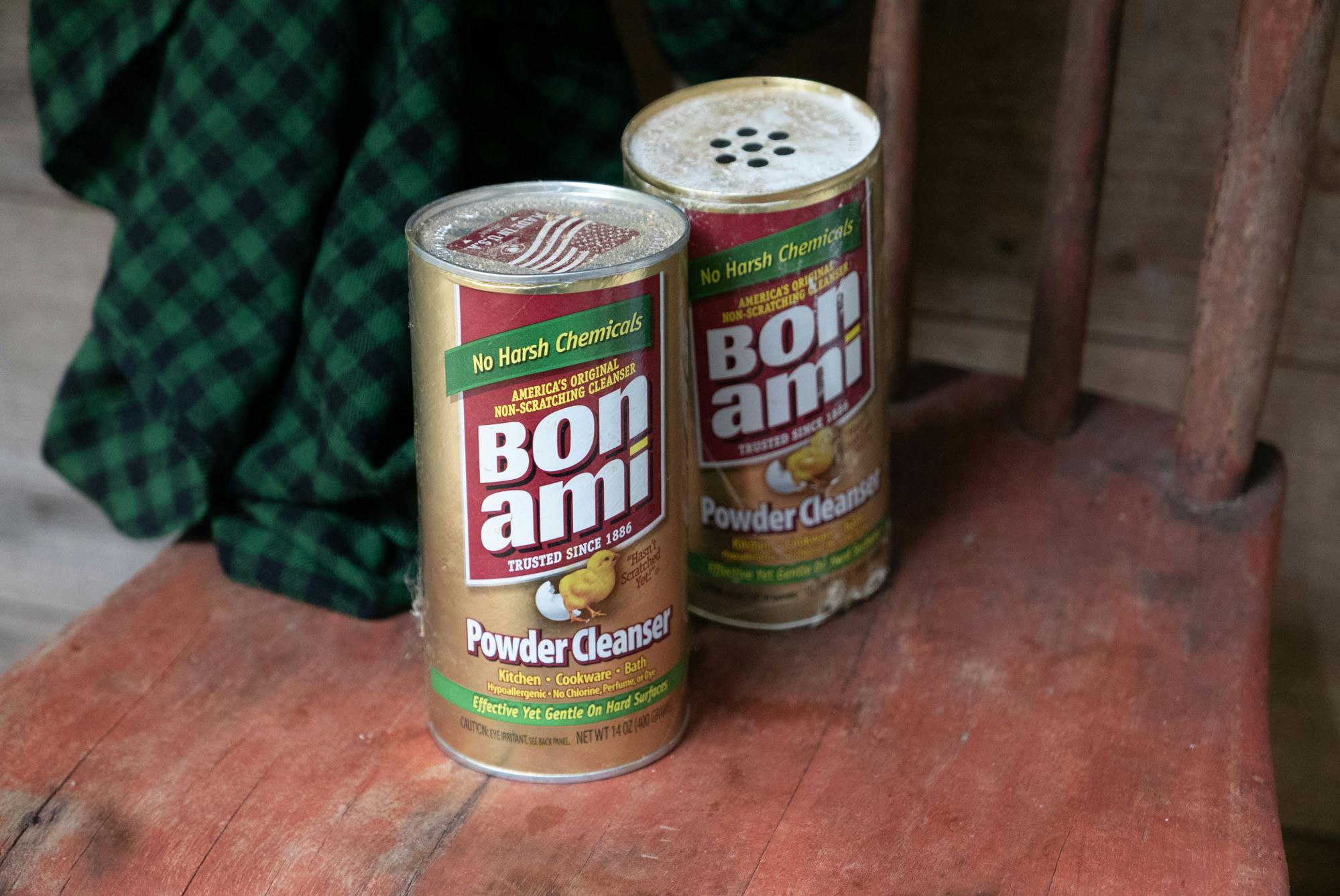 Two cans of Bon Ami sit on a wooden chair. 