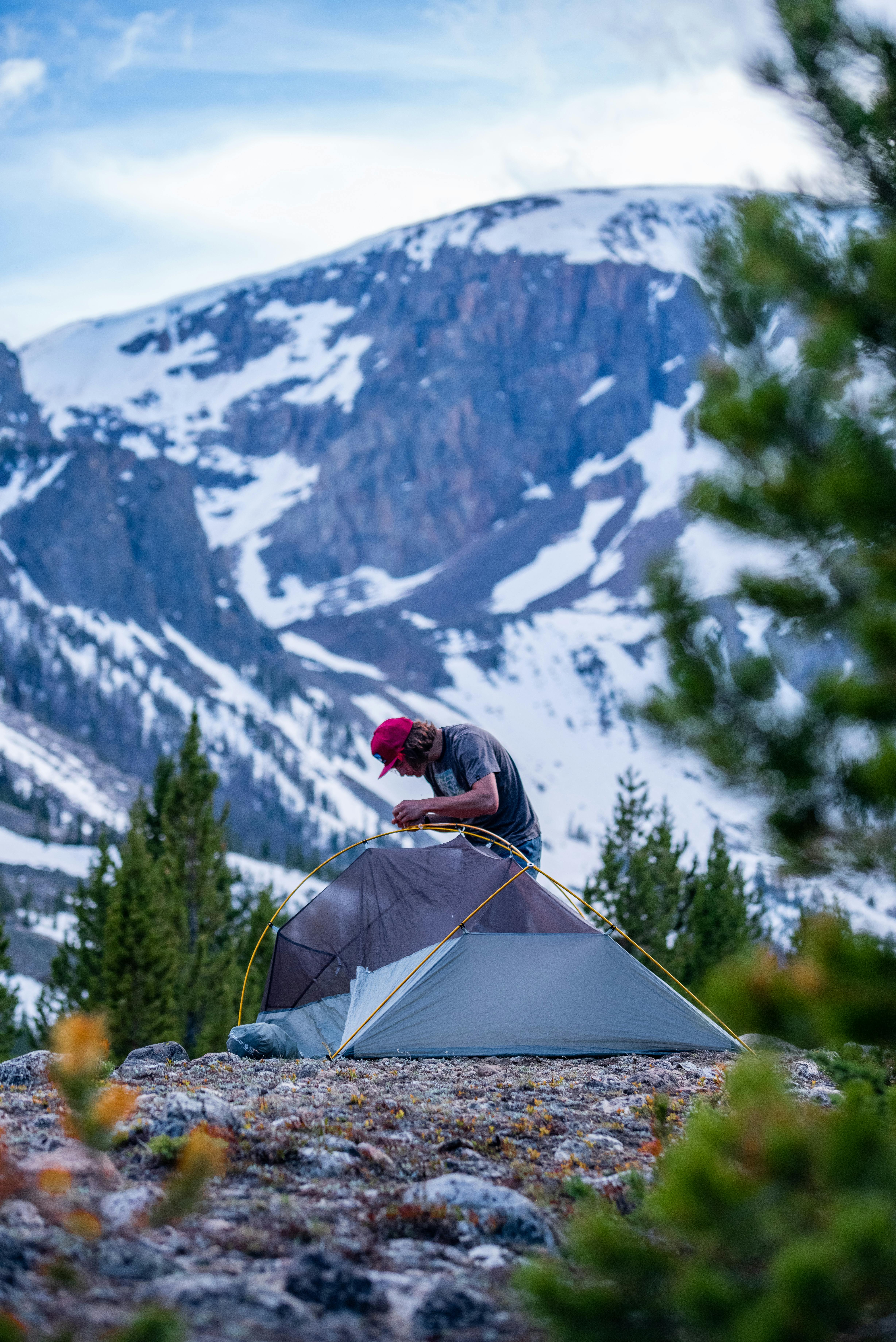 A man in a red hat sets up his tent in the mountains