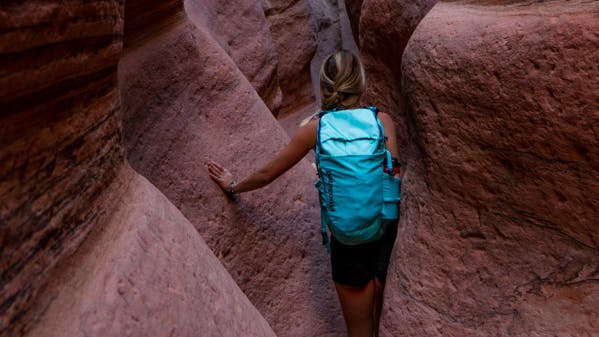 A woman walks through a slot canyon with a backpack on.