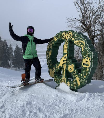 A snowboarder standing next to a peace sign in the snow. 