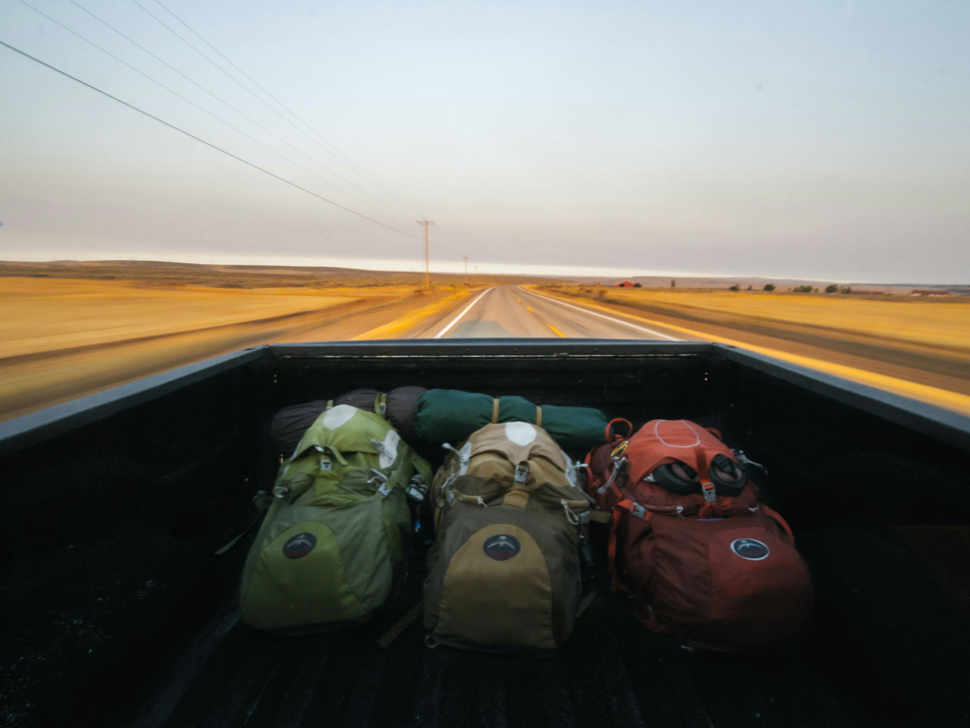 Three backpacks and sleeping pads in the back of a pickup truck