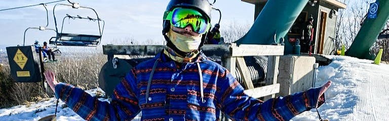 A snowboarder standing in front of a chairlift with the  Giro Contact Goggles on. 