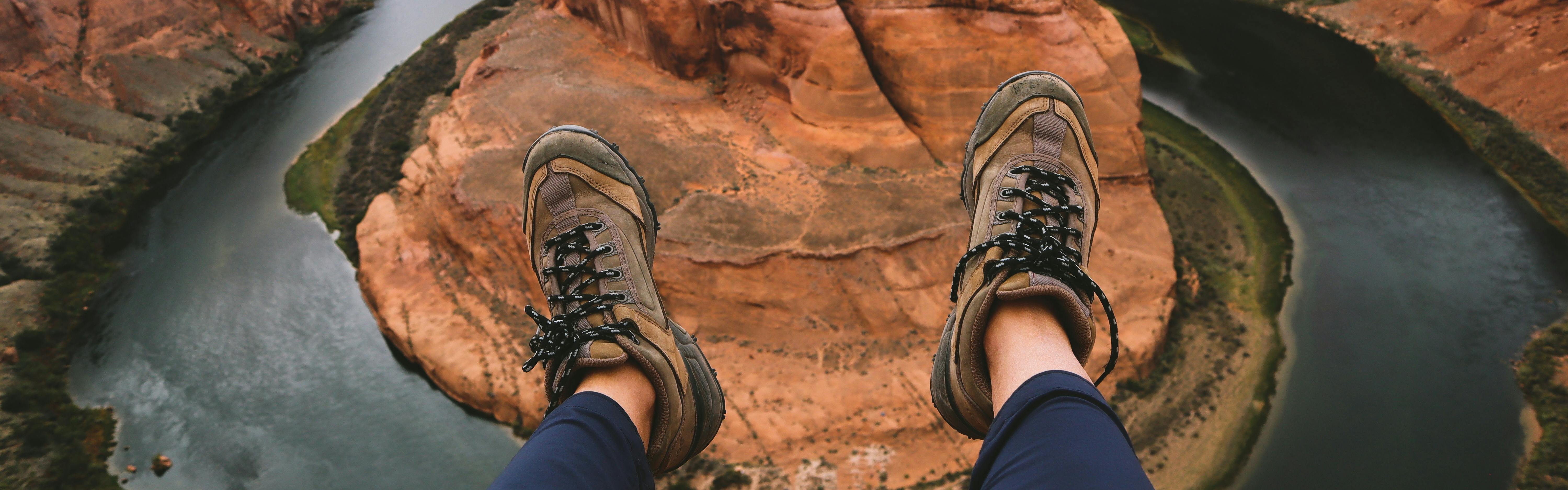 Two feet wearing hiking boots extend over a rounded river gorge