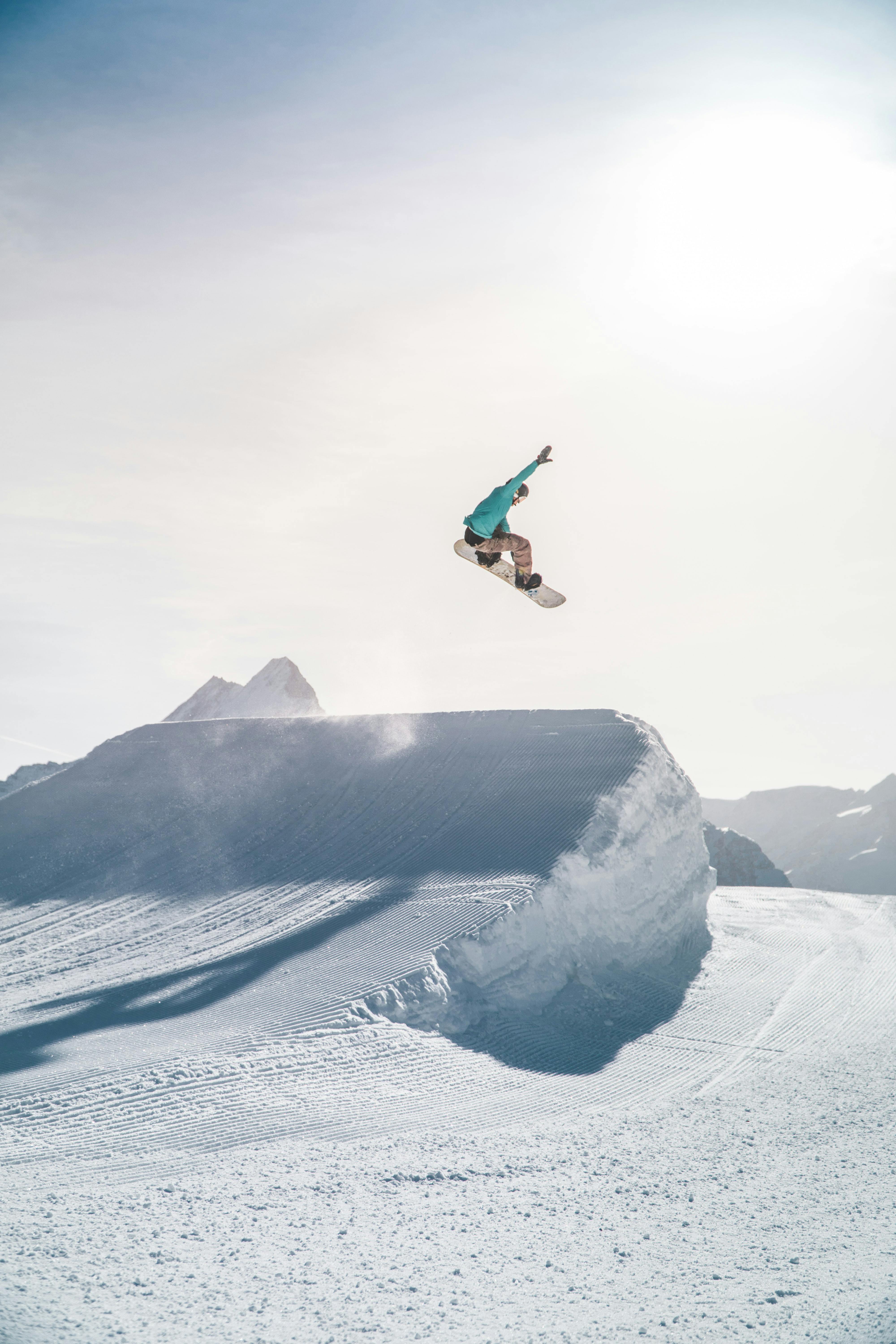 Snowboarder is in the air after riding off a tall jump. He grabs his snowboard with one hand and the other hand is in the air. 