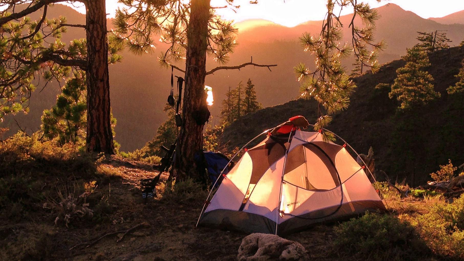A tent is illuminated by the sun on a ridge.