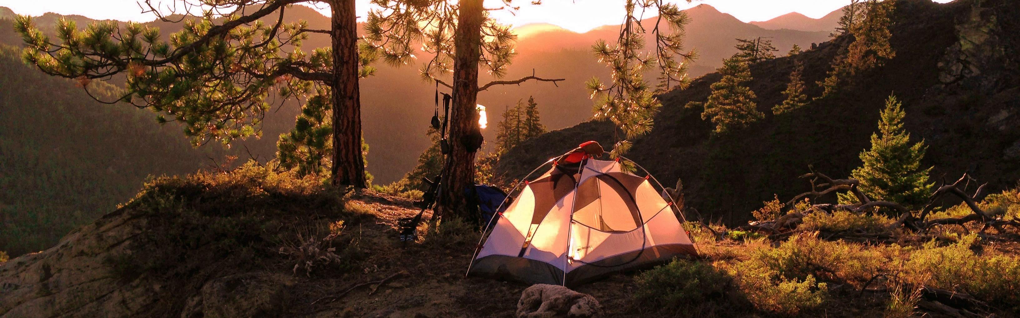 A tent is illuminated by the sun on a ridge.