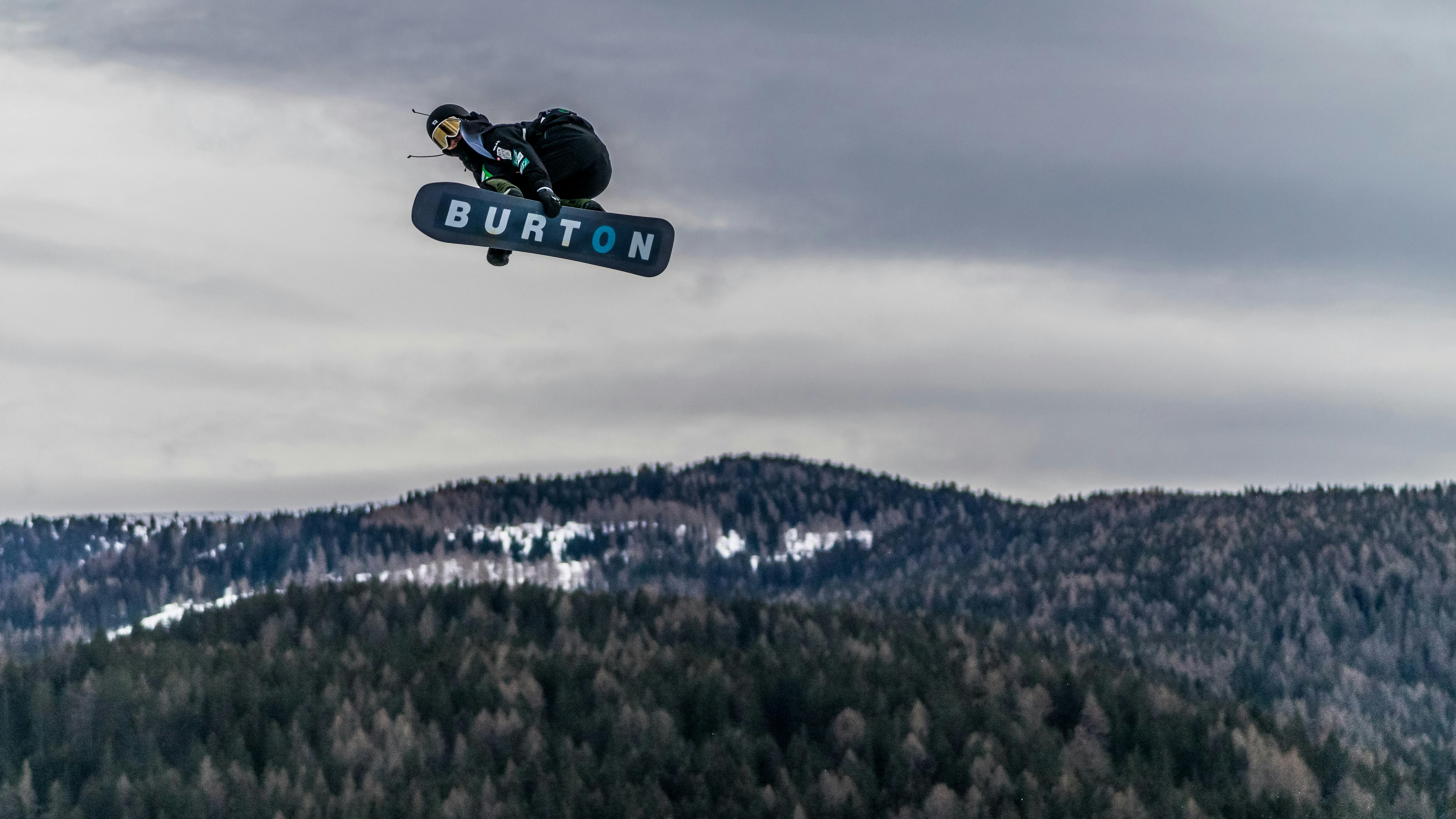 A snowboarder flies through the air with mountains in the background