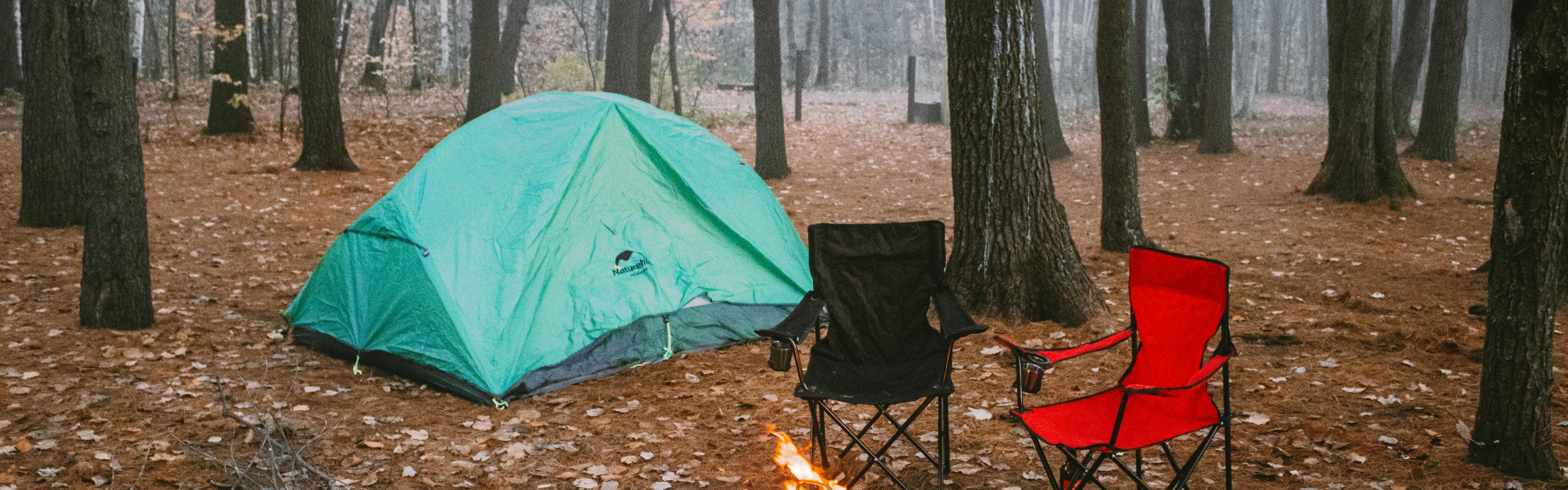 A tent in the rain. There are some camp chairs sitting around a fire pit near the tent.