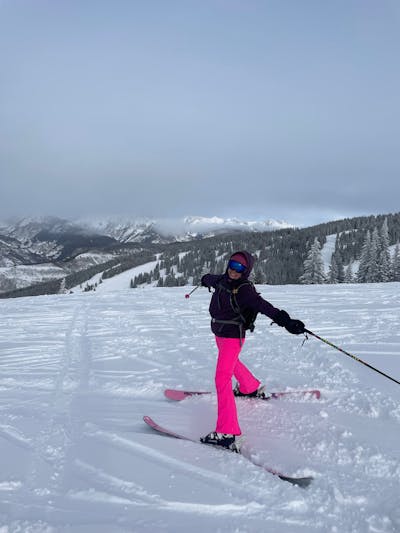 A woman stands on her skis with her arms open looking at the camera. There is a lot of snow in the background. 