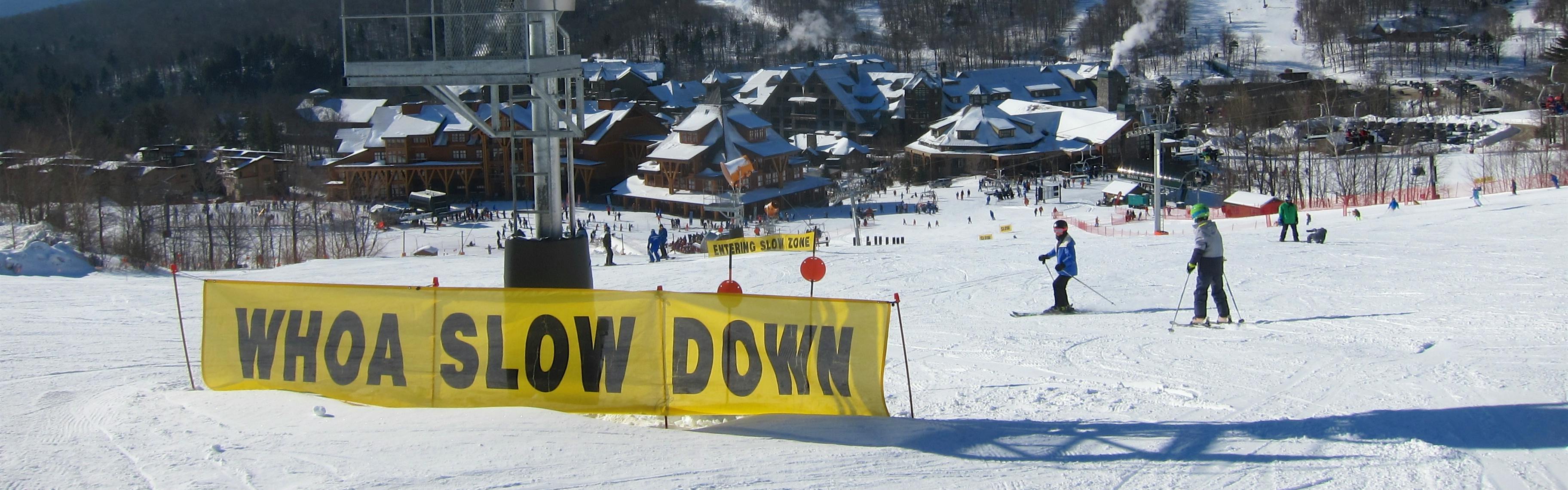 A large yellow sign at a ski resort reads "Woah Slow Down."