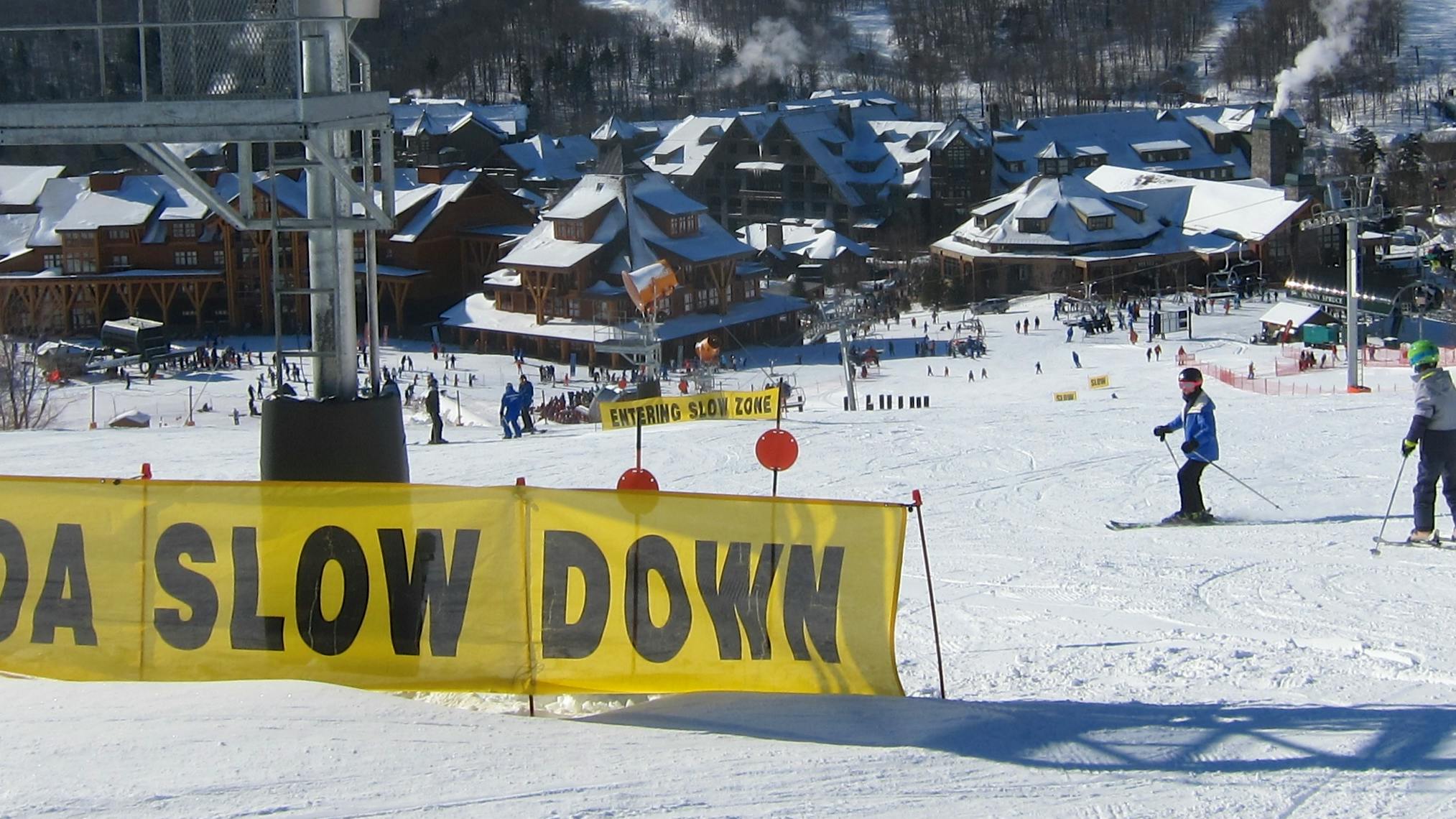A large yellow sign at a ski resort reads "Woah Slow Down."