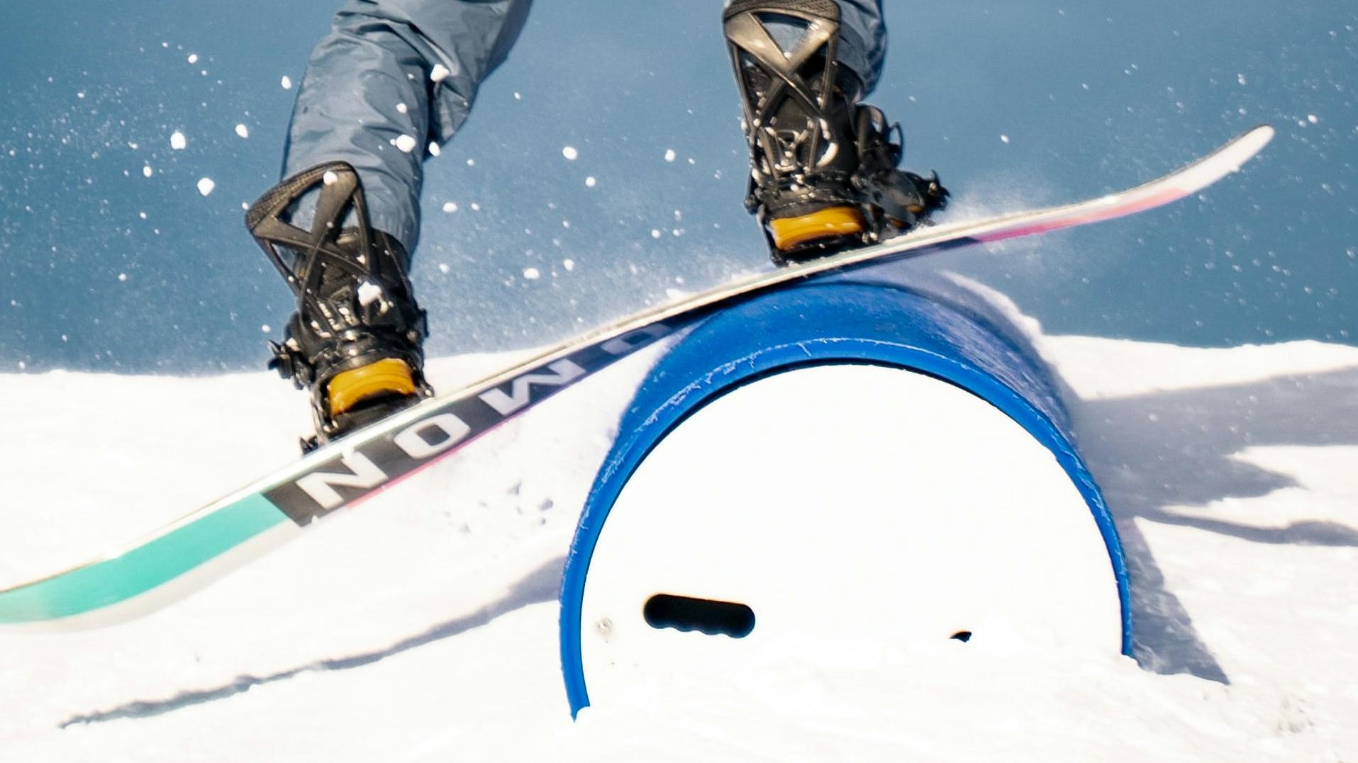 A snowboarder rides a board over a blue tube-like rail. 