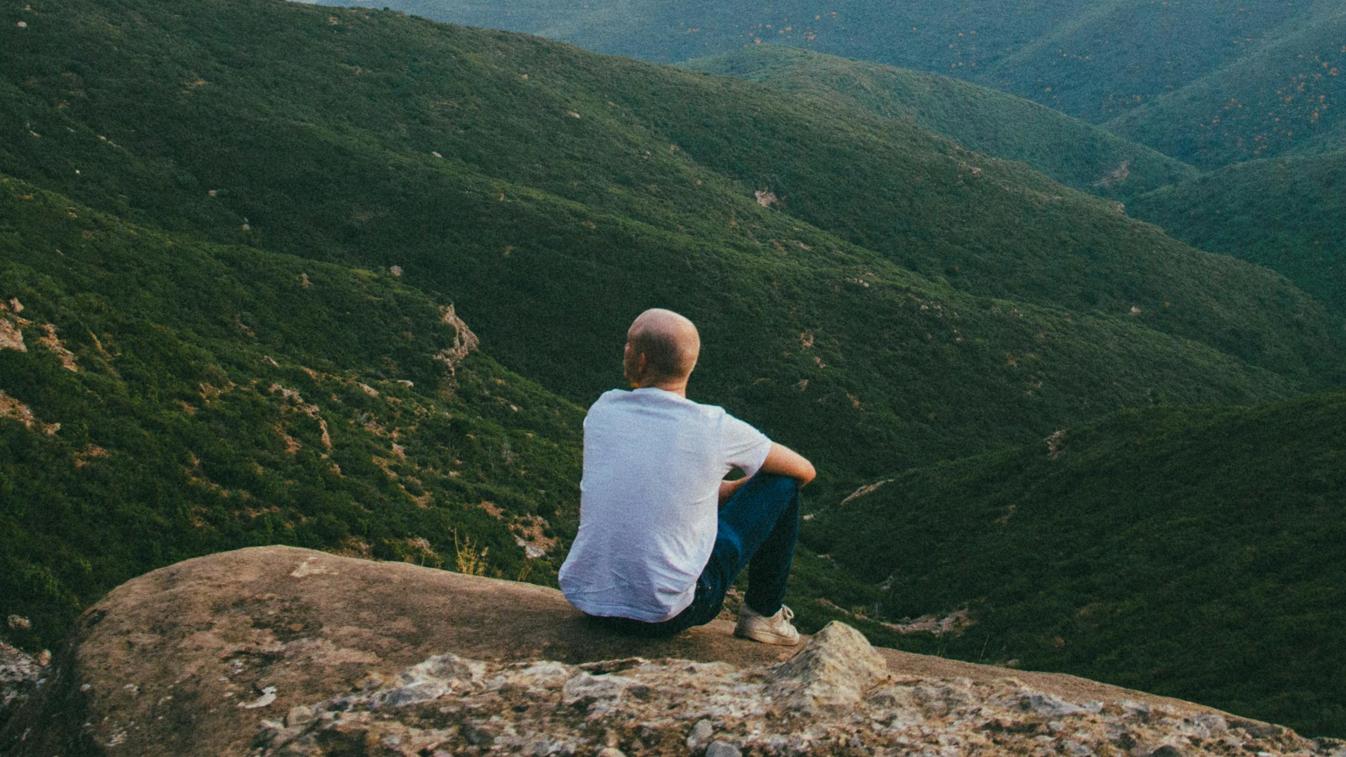 A man sitting on a rock looking out at the green valley below