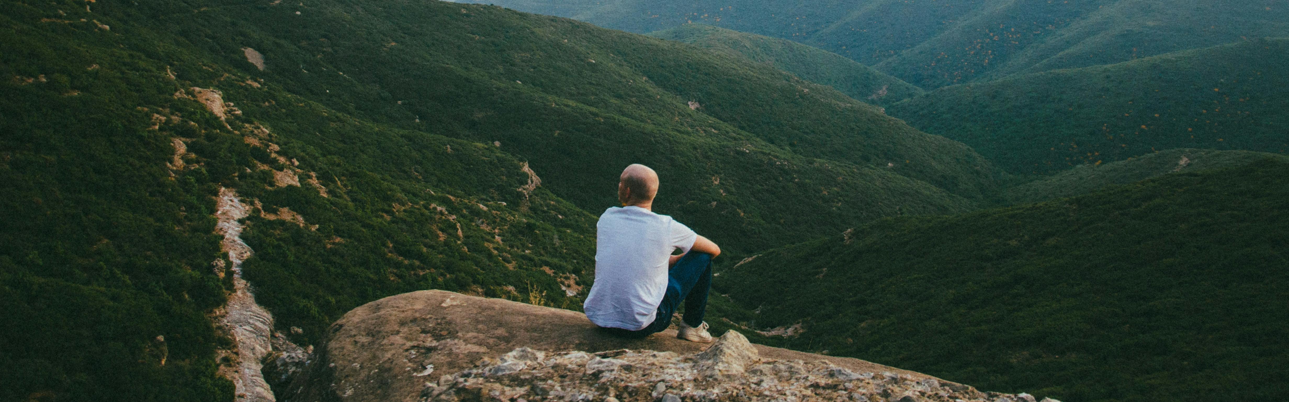 A man sitting on a rock looking out at the green valley below