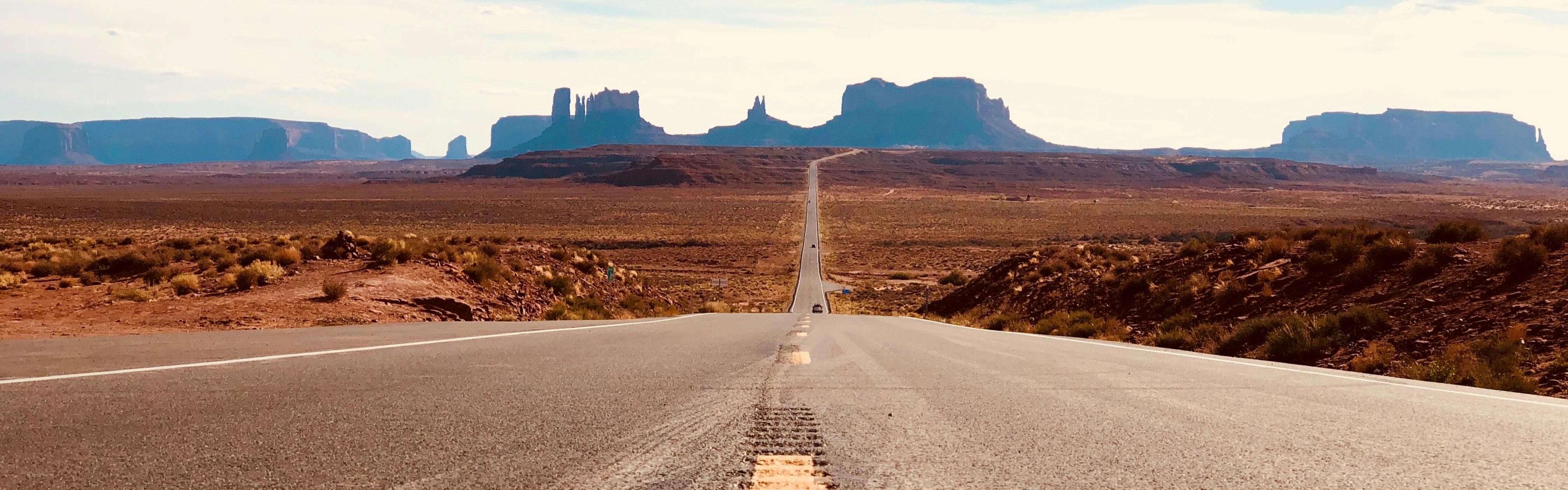 A straight road extends into the distance where buttes and mesas rise up.