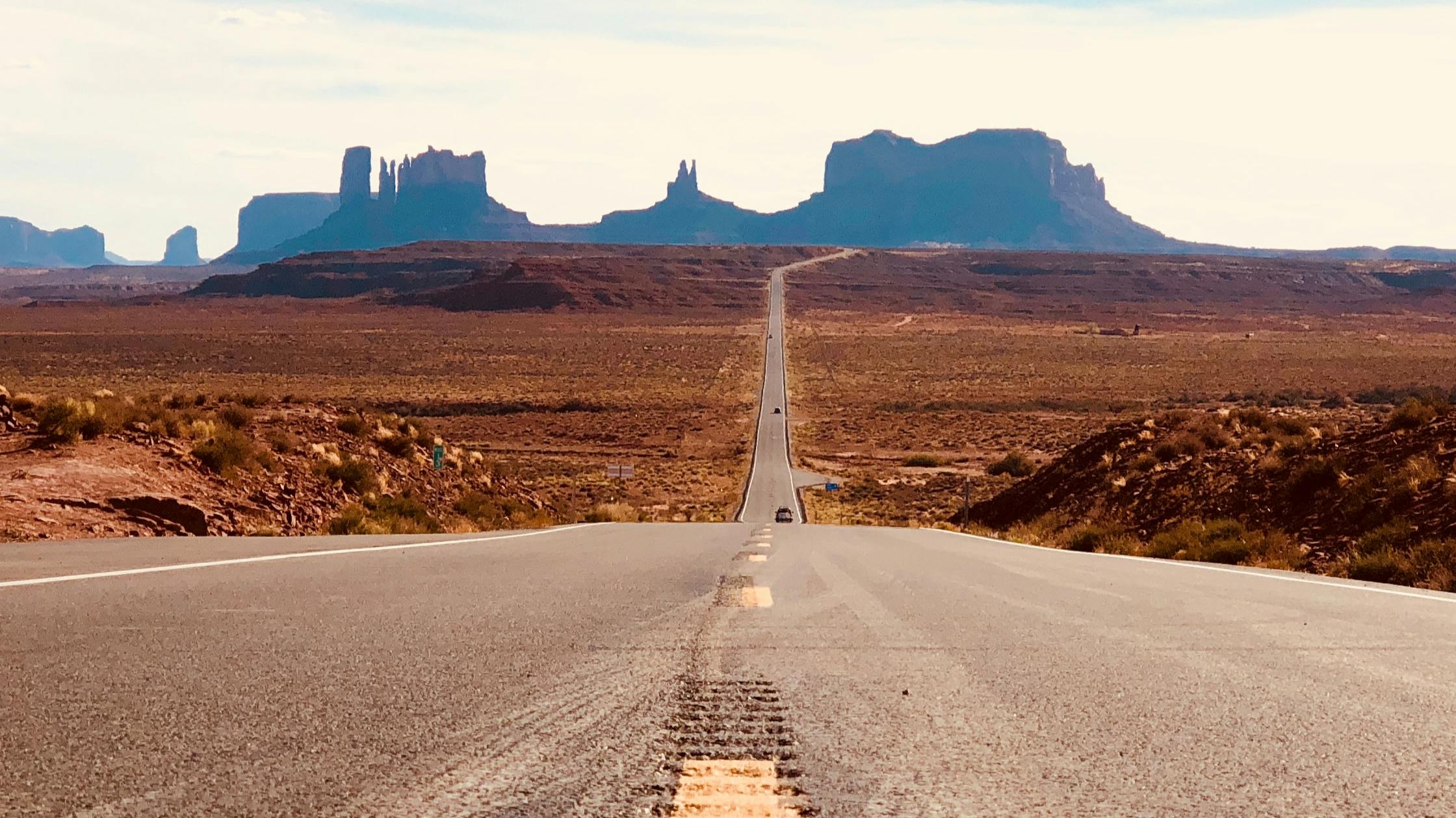 A straight road extends into the distance where buttes and mesas rise up.
