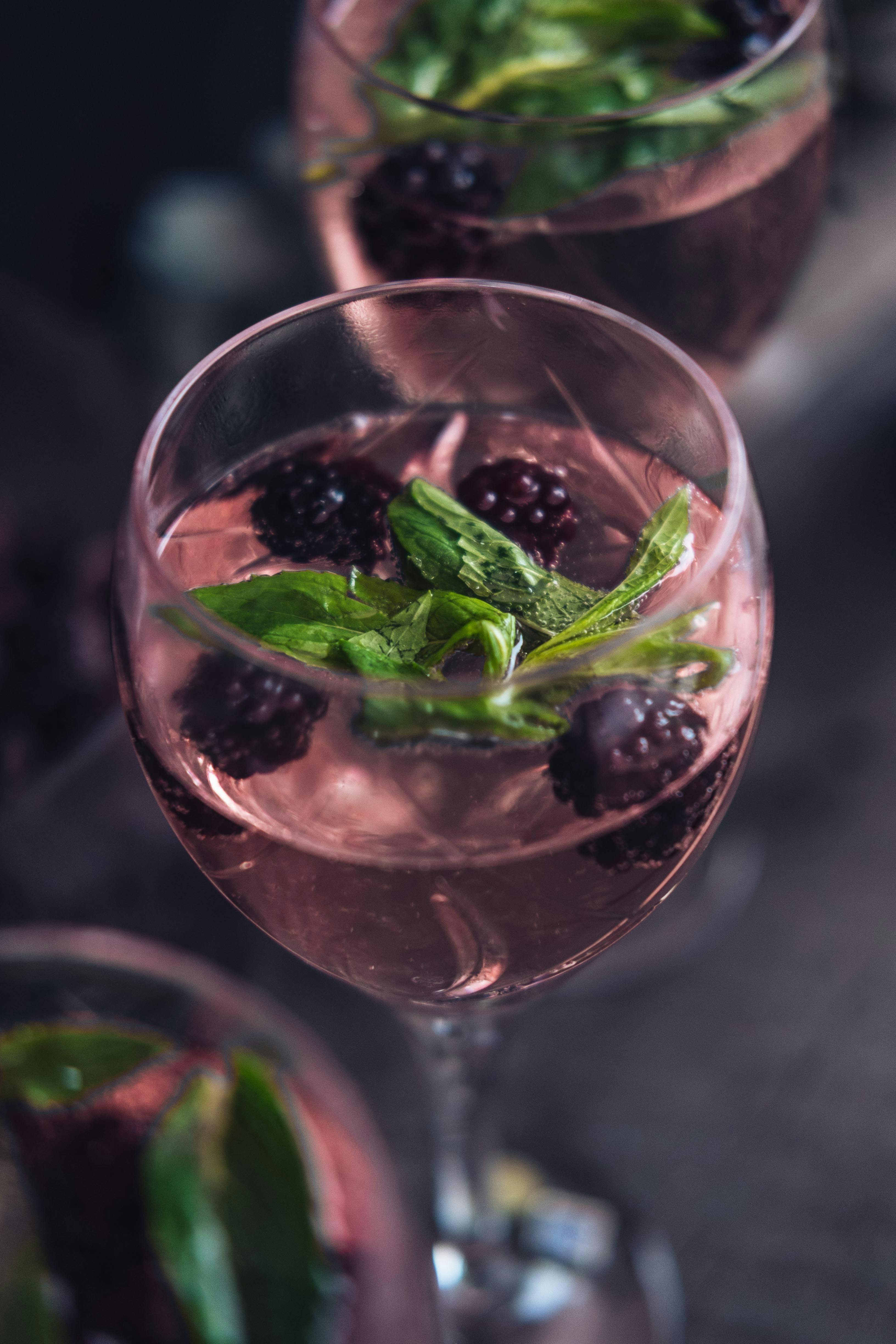 A drink in a wine glass with blackberries and mint.