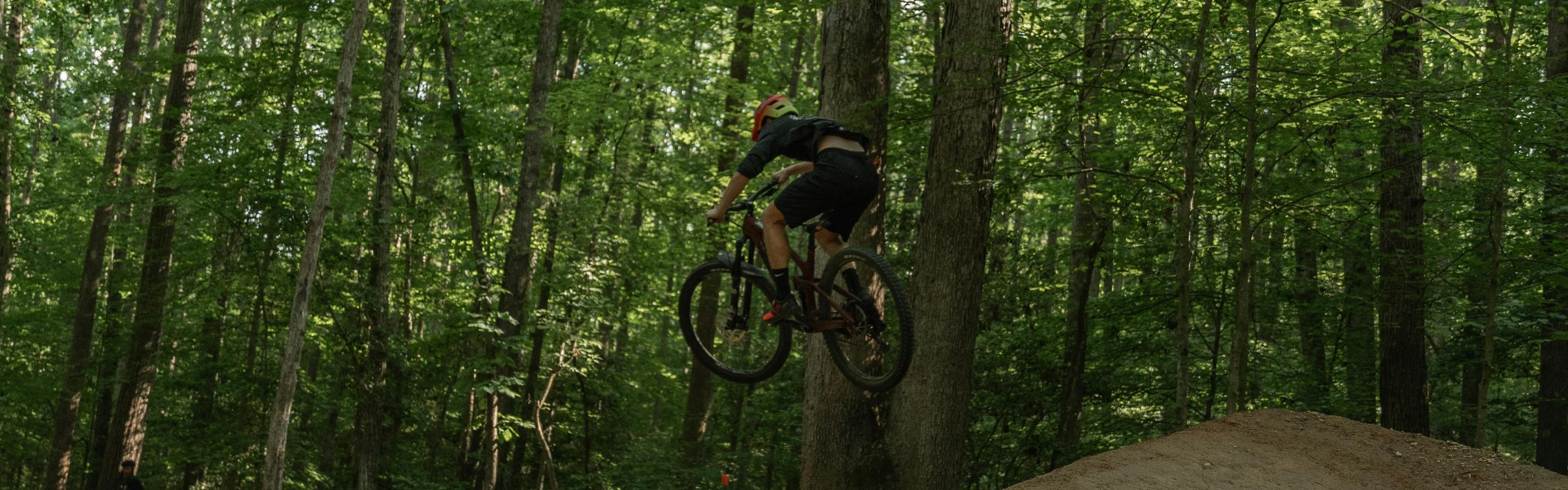 A mountain biker jumps off a dirt jump in a forest.