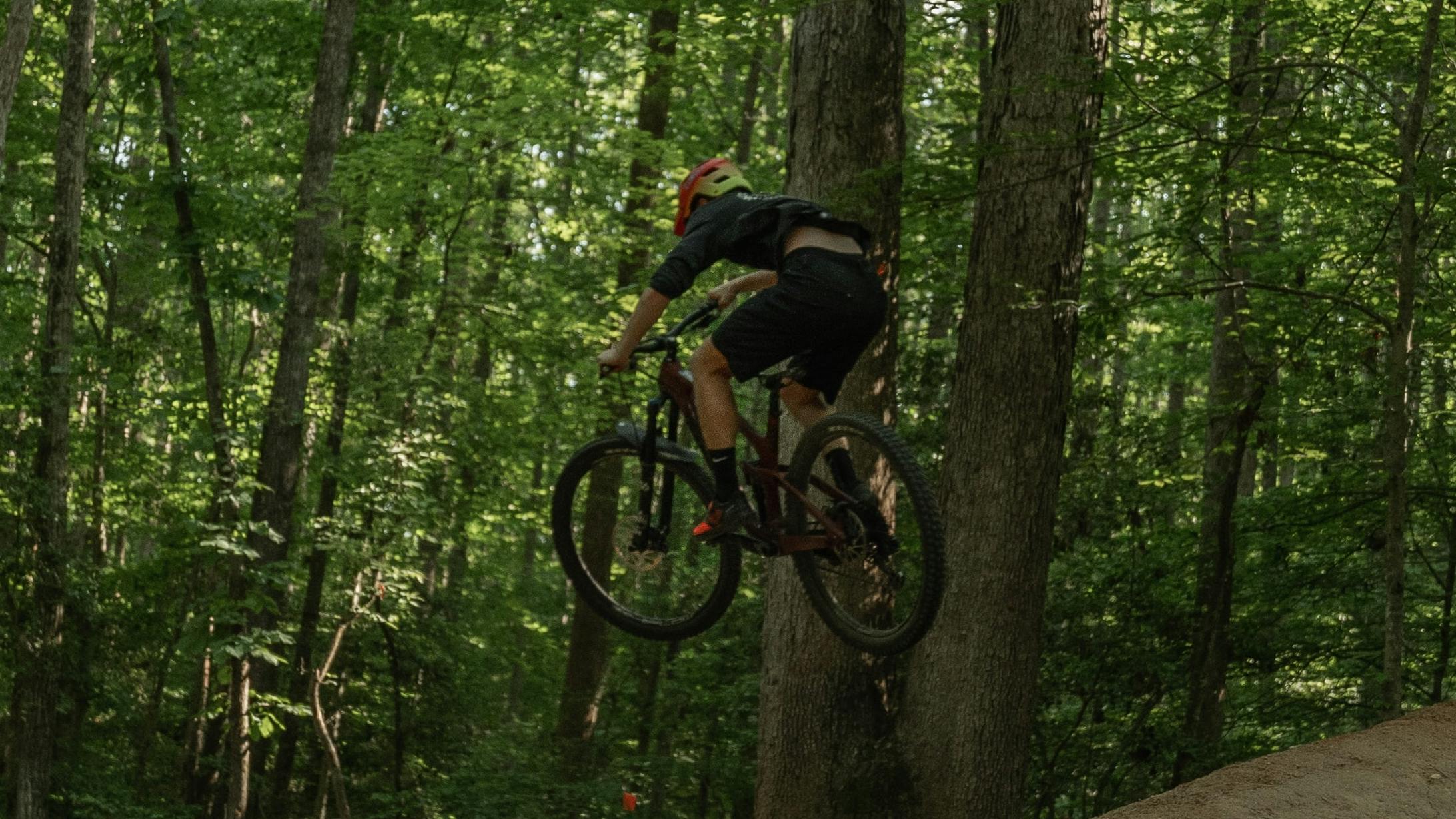 A mountain biker jumps off a dirt jump in a forest.