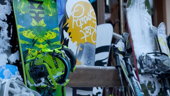 Several snowboards sit against a snowboard holder outside a lodge. There are yellow, green, and blue snowboards.