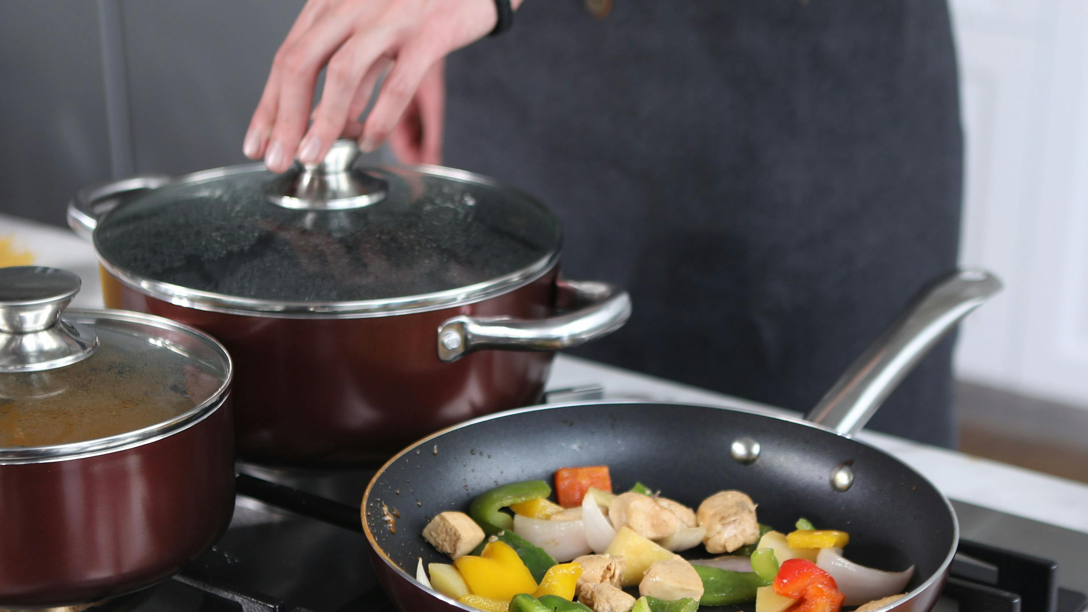 A person cooking some vegetables in a pan and some other foods in a pot over a stove.