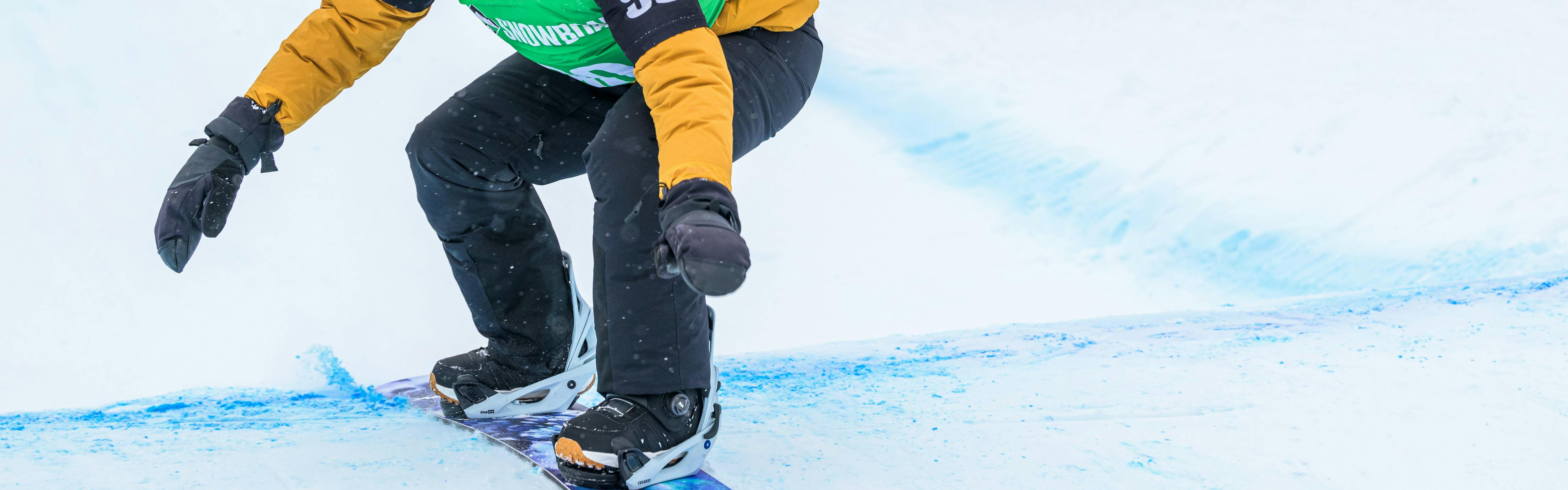 Rider in yellow jacket and green racing bib pumping over the roller section of a banked slalom course.