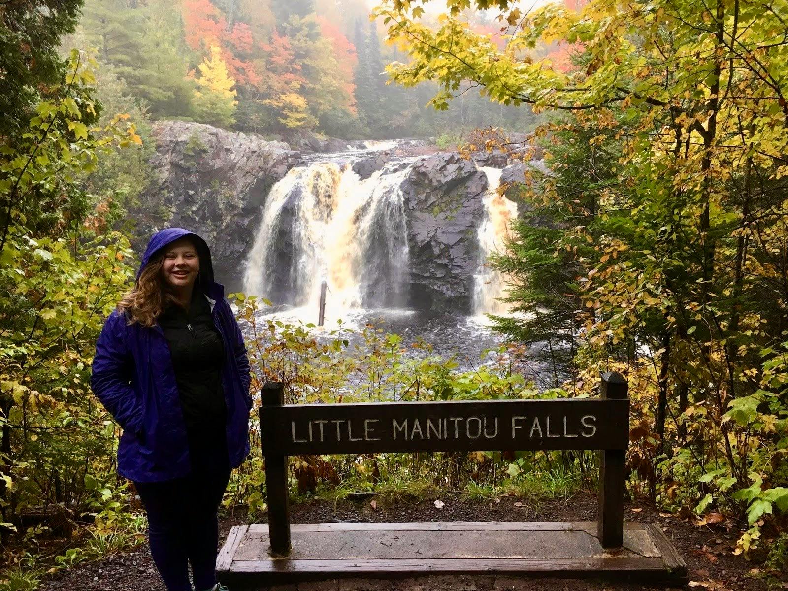 The author stands and smiles in a raincoat in front of Little Manitou Falls in Pattison State Park. 