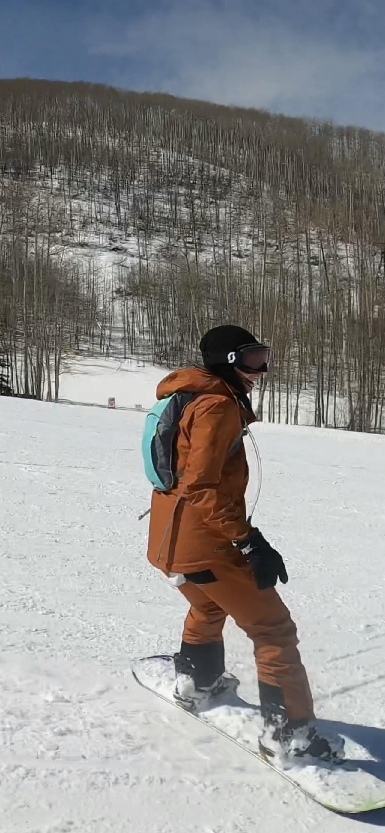 A woman with torn snowboard pants snowboards down a hill.