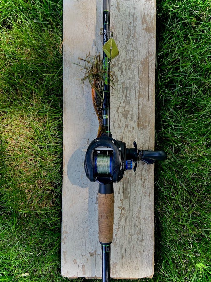 The author's rod and reel set-up sits on a plank of wood. A buzzbait lure is attached to the line. 