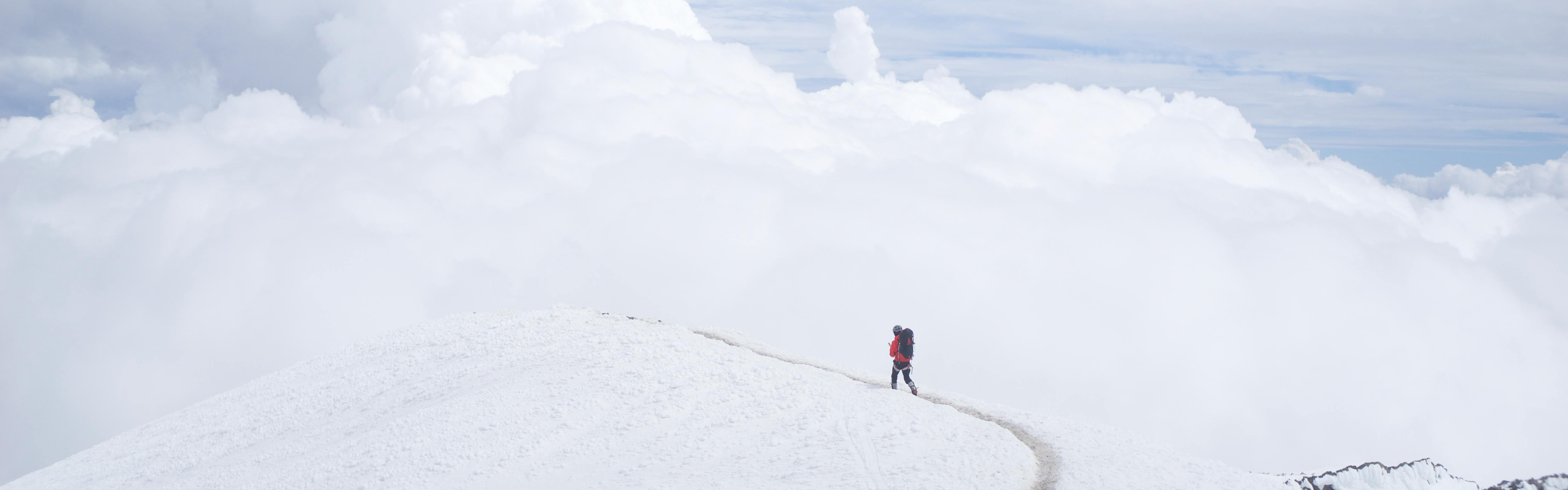 Someone walks across a snowy expanse with clouds or fog rising in the background so it's not clear where the landscape ends and the sky begins.
