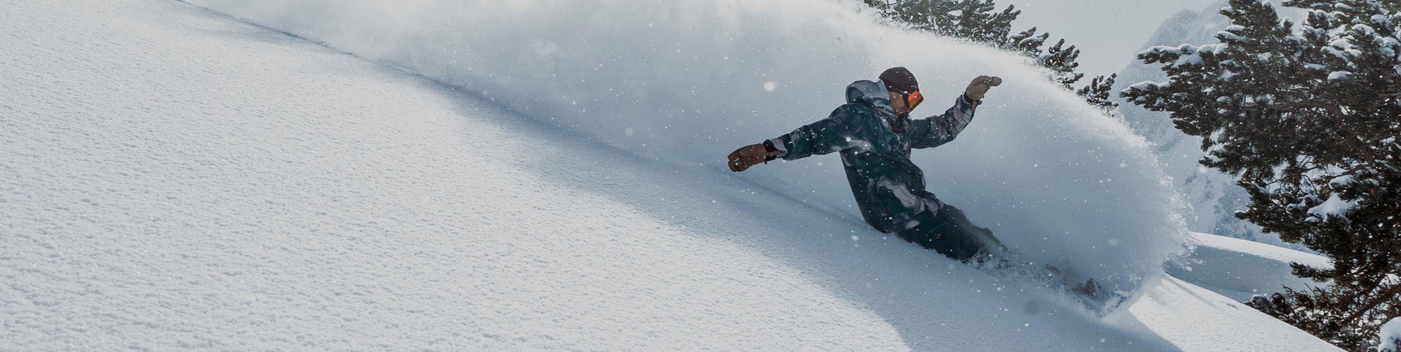 A snowboarder is shown brushing up a lot of snow on a mountain