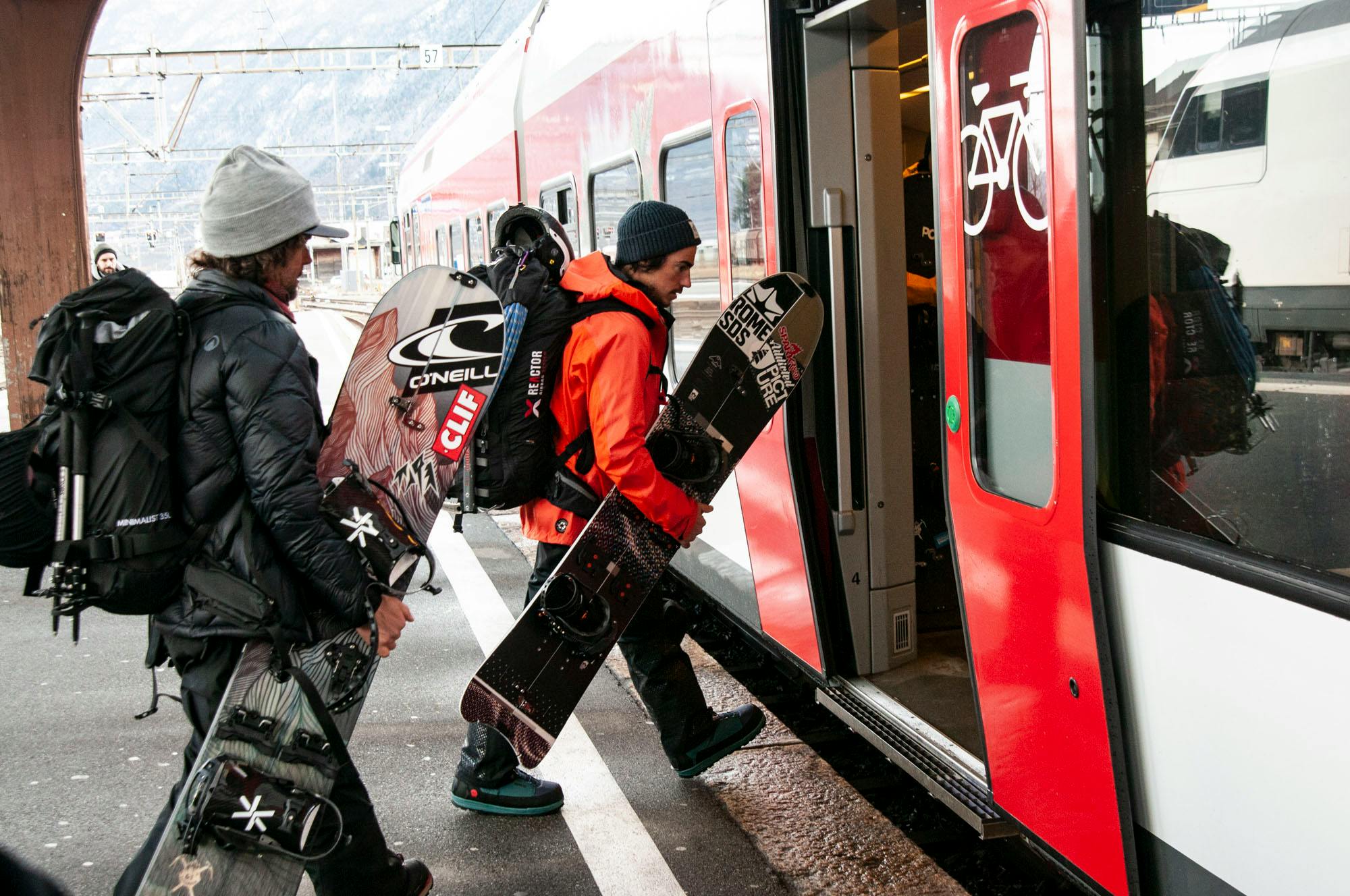 Two snowboarders carrying their boards and boarding a subway car
