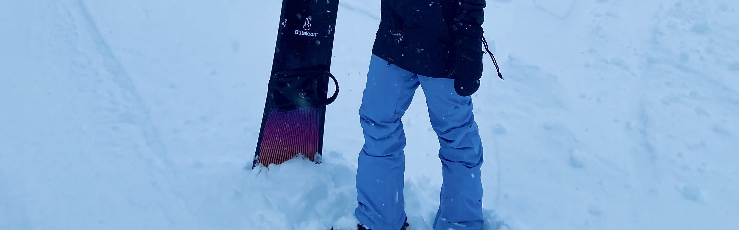 A woman stands in the snow with her snowboard wearing the Burton Avalon GORE-TEX Bib pants.