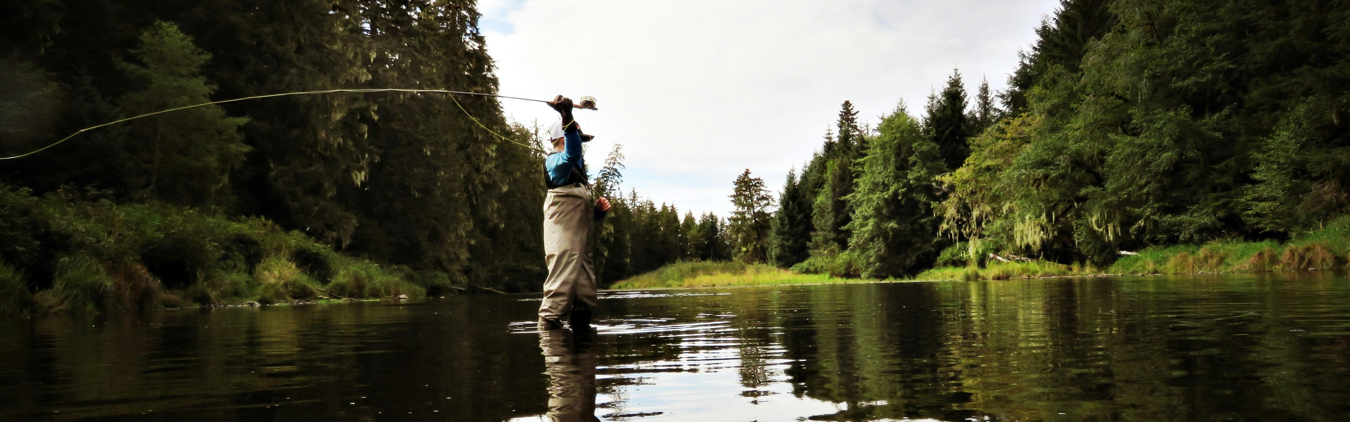 A man in waders casts a fly fishing rod