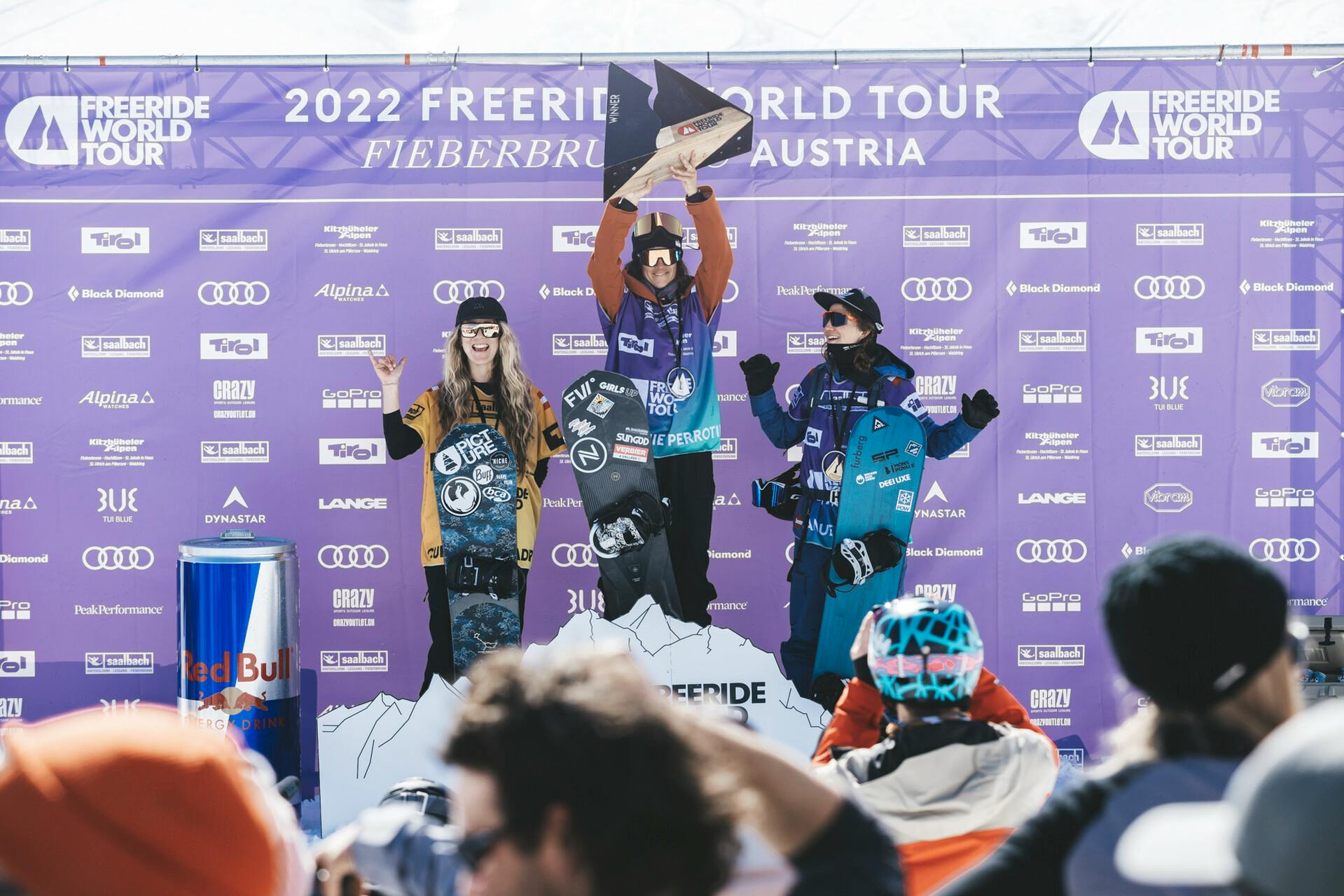 The top three female snowboards of Stop Four of the FWT stand on the podium in front of a purple backdrop.