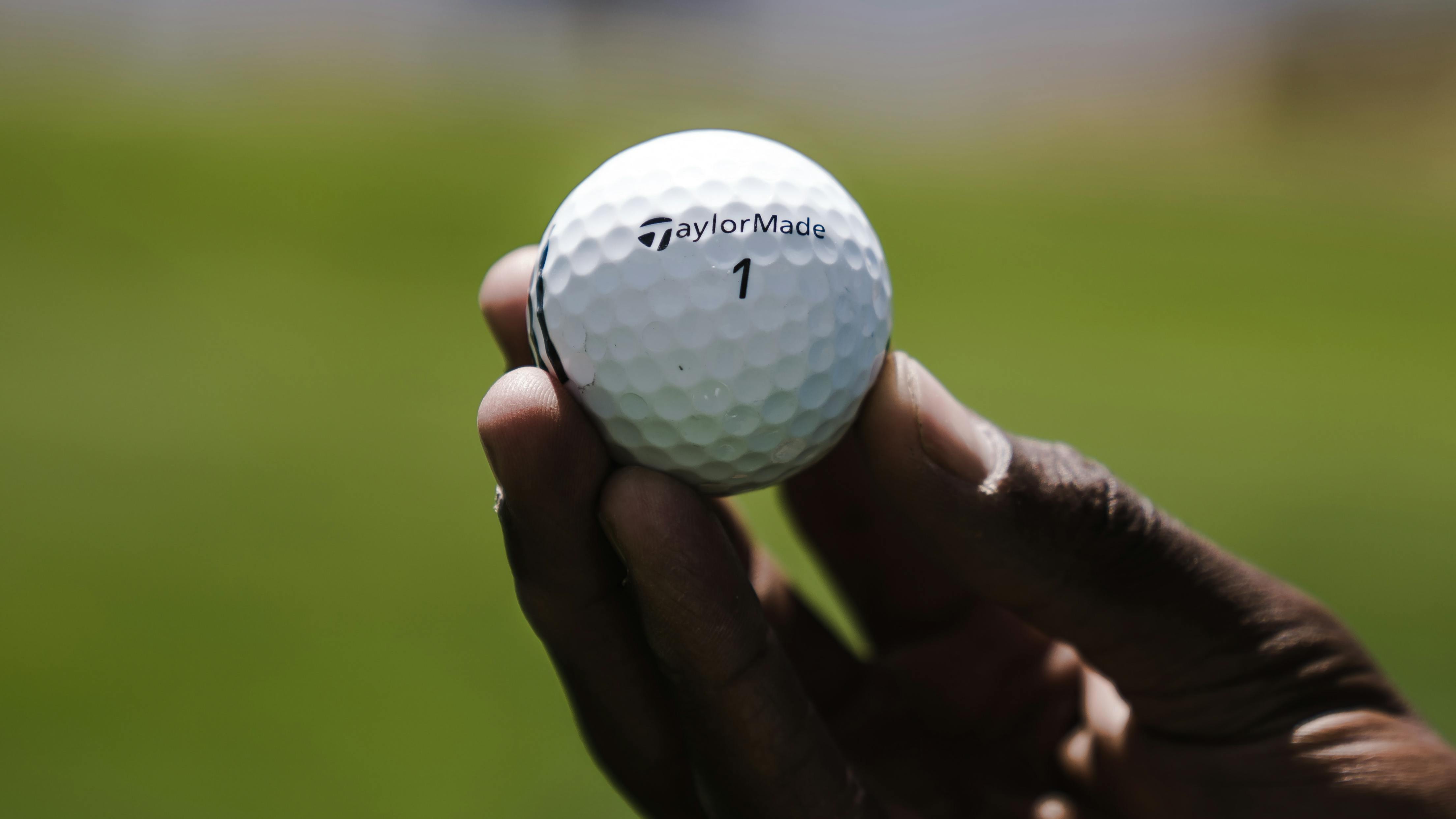 A hand holding a Taylormade Golf ball. 