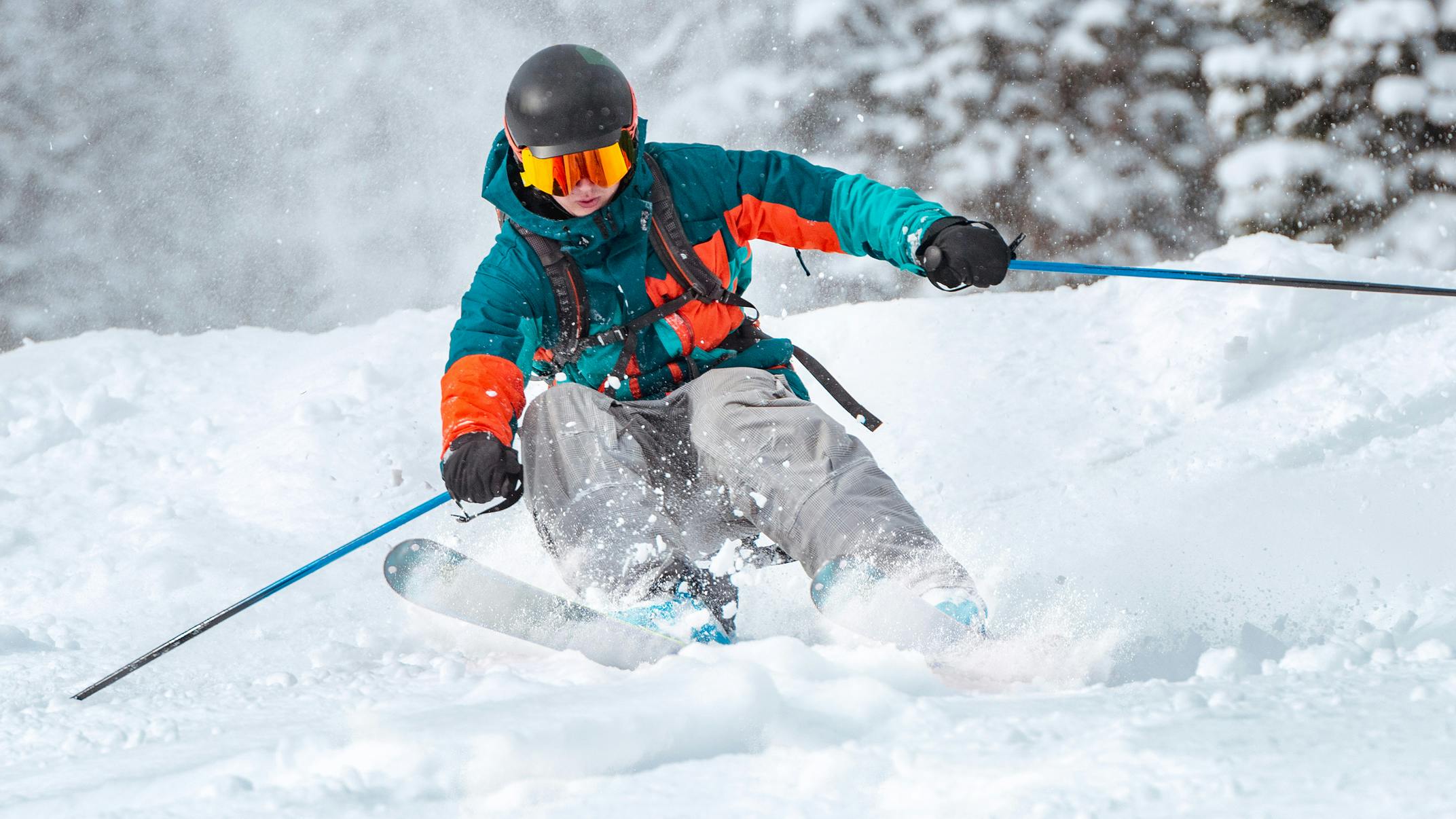 A skier in grey pants and a turquoise jacket races through the snow