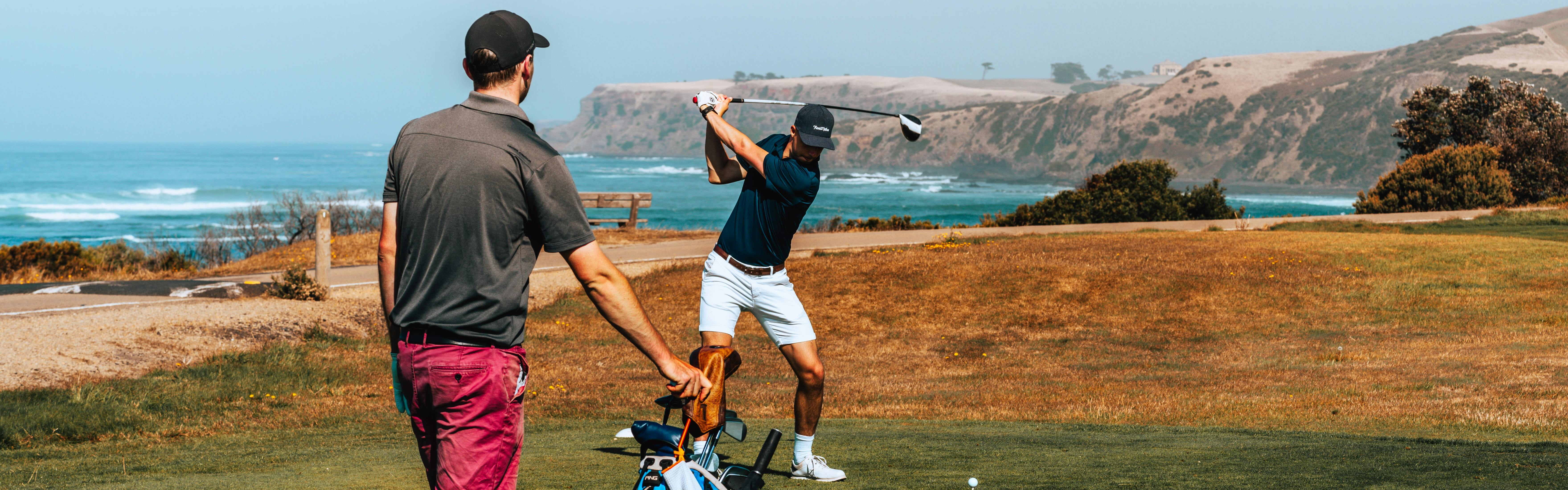 Two men golf on a course overlooking the ocean.