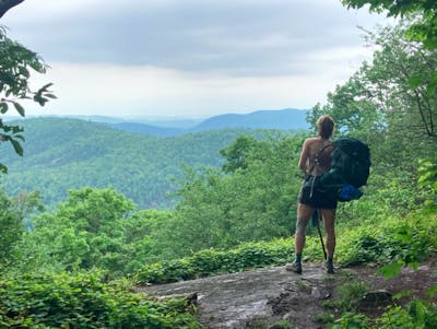 A woman taking off her backpacking backpack on a trail. 
