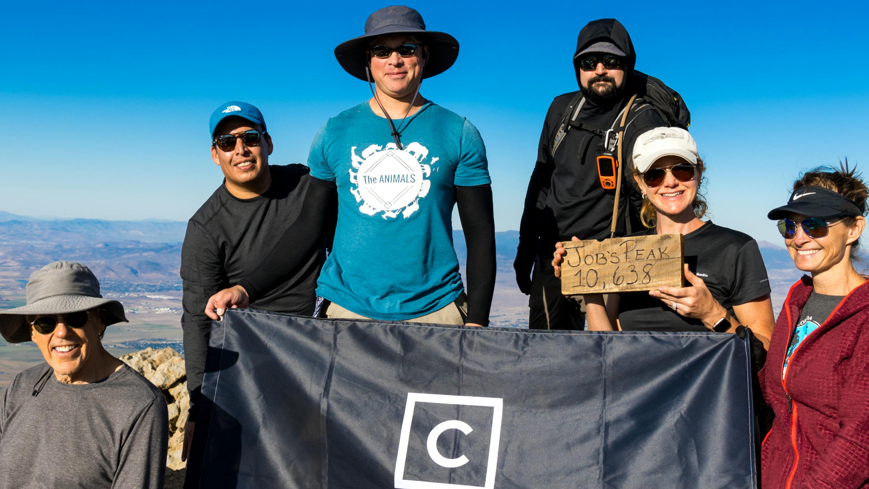 A group of people from Tahoe Aventures gathers on the top of Job's Peak for a picture with a black Curated flag.