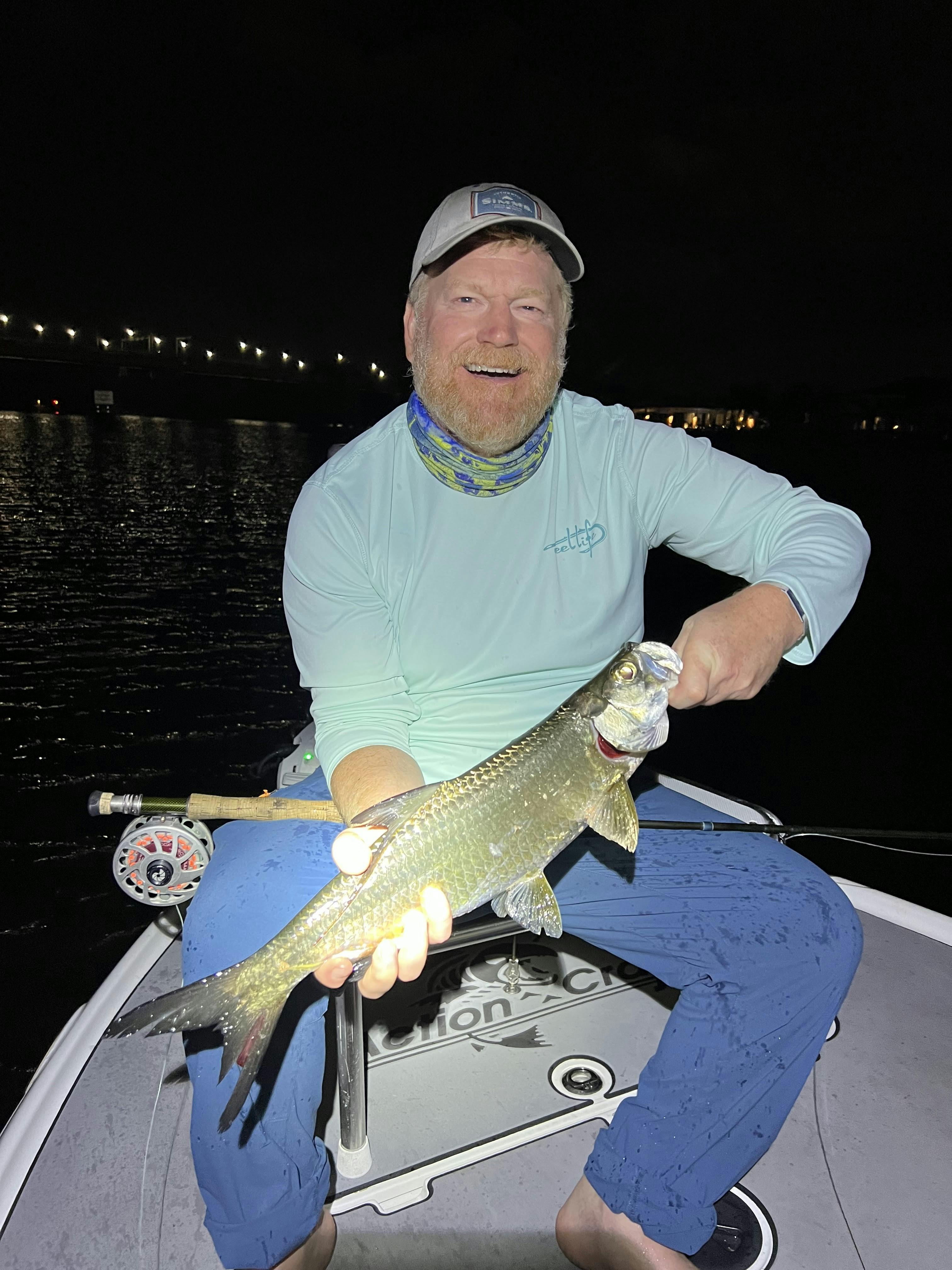 A man on a boat holding a fish. It is nighttime. 