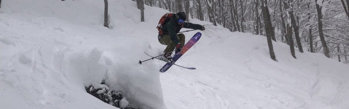 A skier grabs his ski as he jumps off a feature.