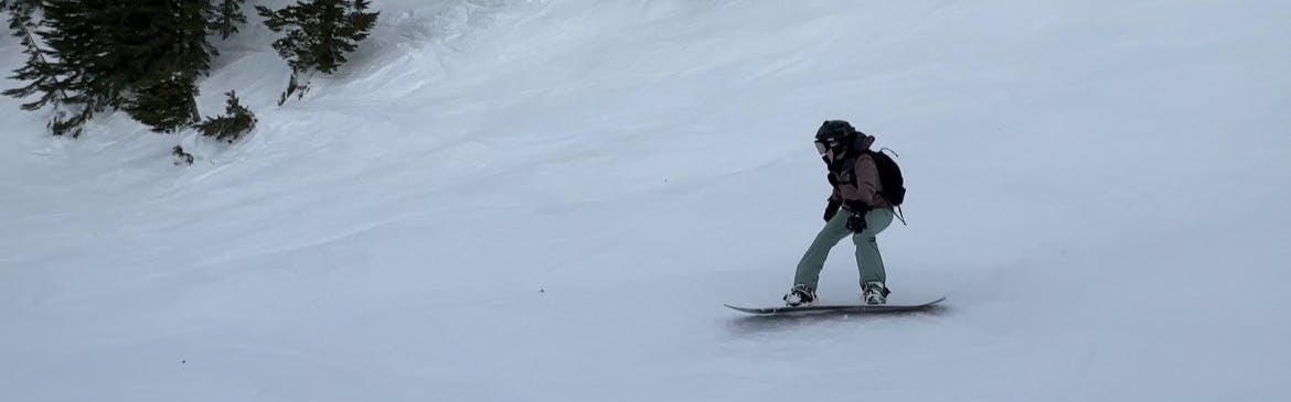 A snowboarder turning down a snowy hill. 