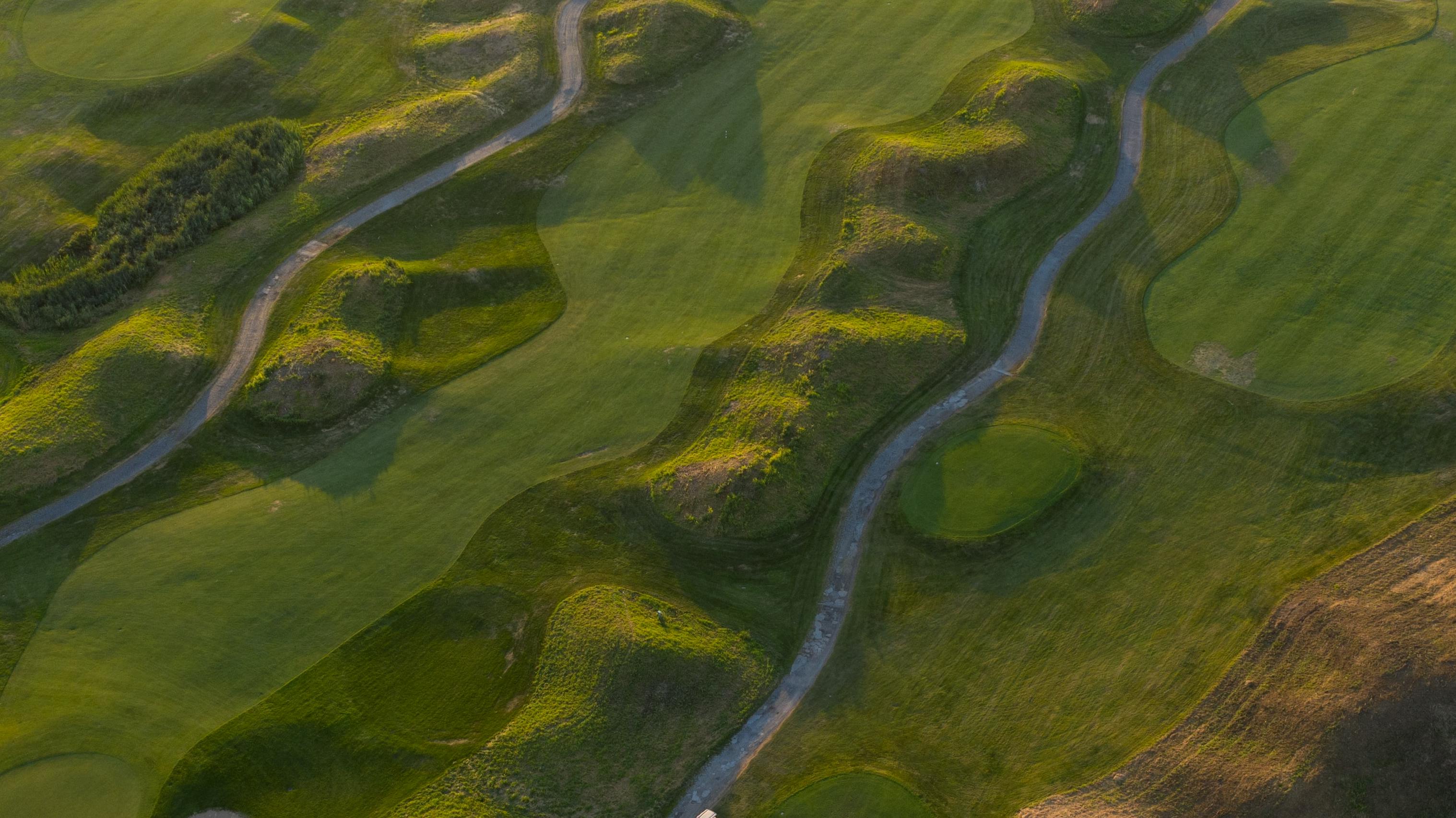 Sky view of a golf course where you can see many fairways, greens, and golf cart trails. 