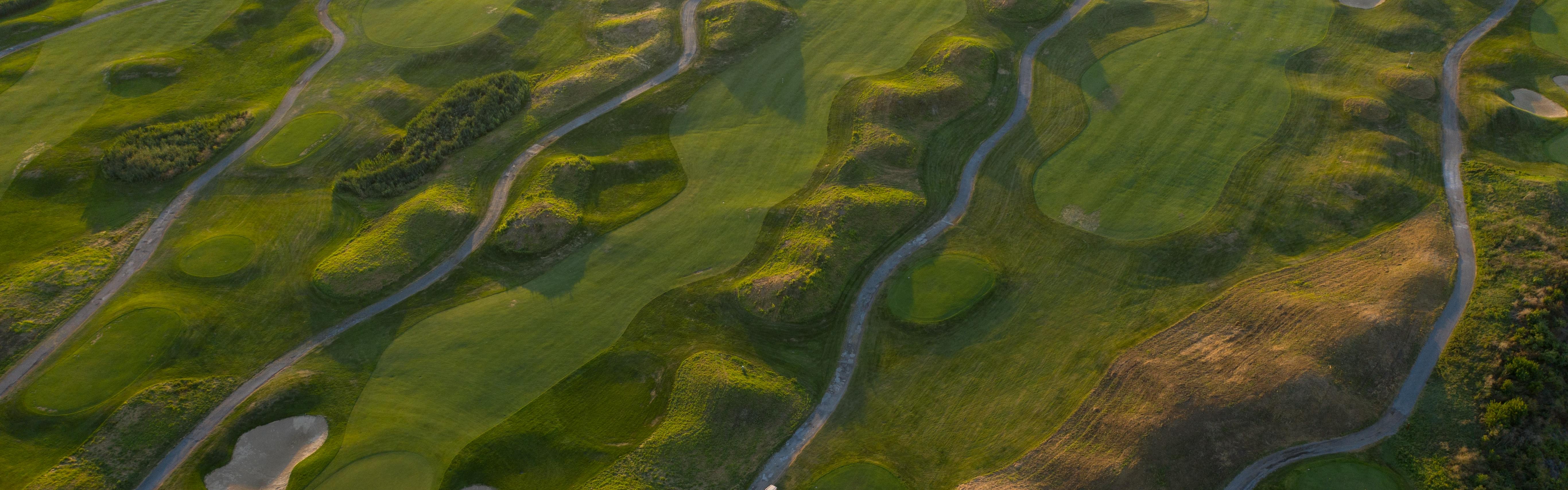 Sky view of a golf course where you can see many fairways, greens, and golf cart trails. 