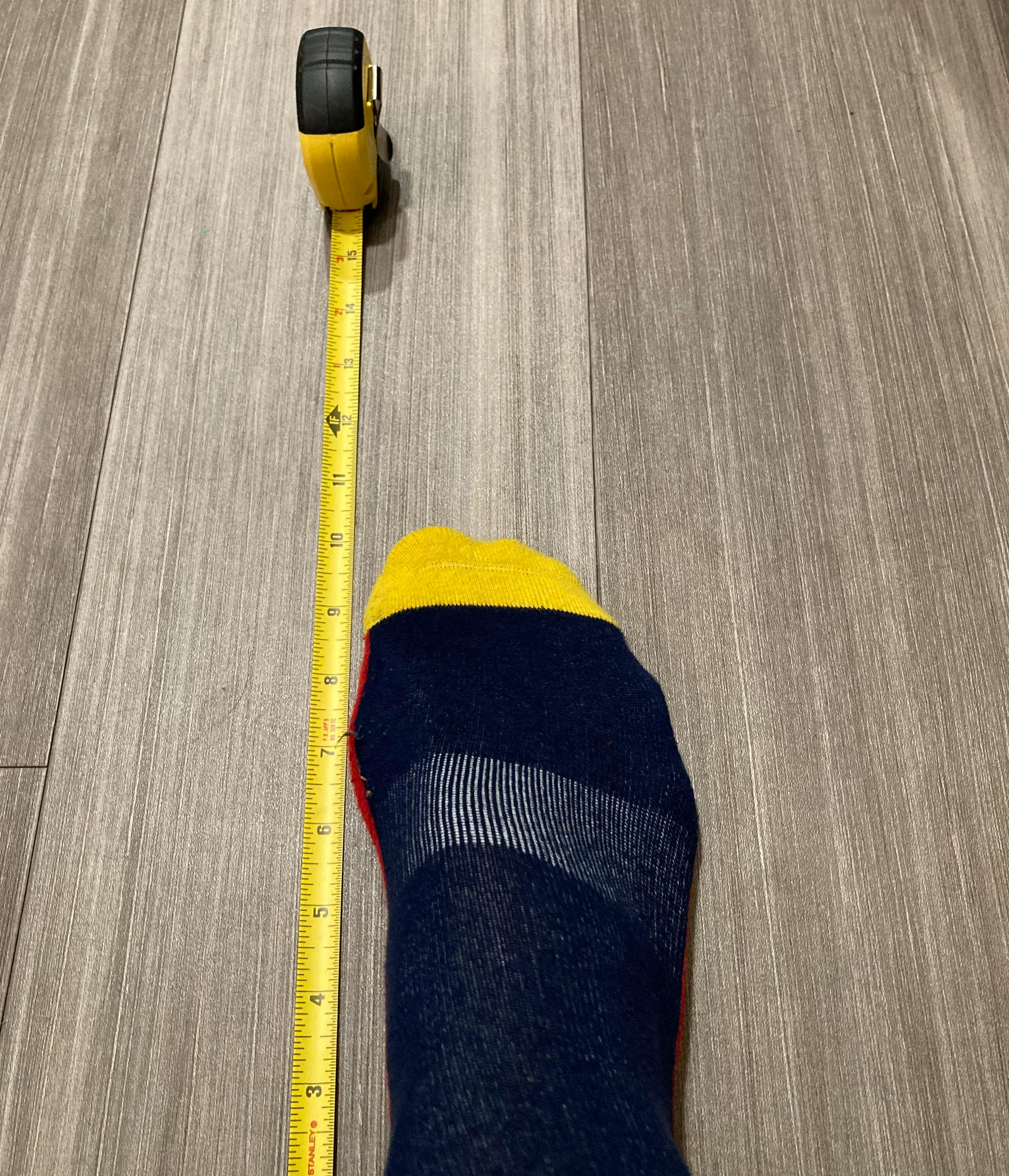 A socked foot lined up next to a spread out tape measure