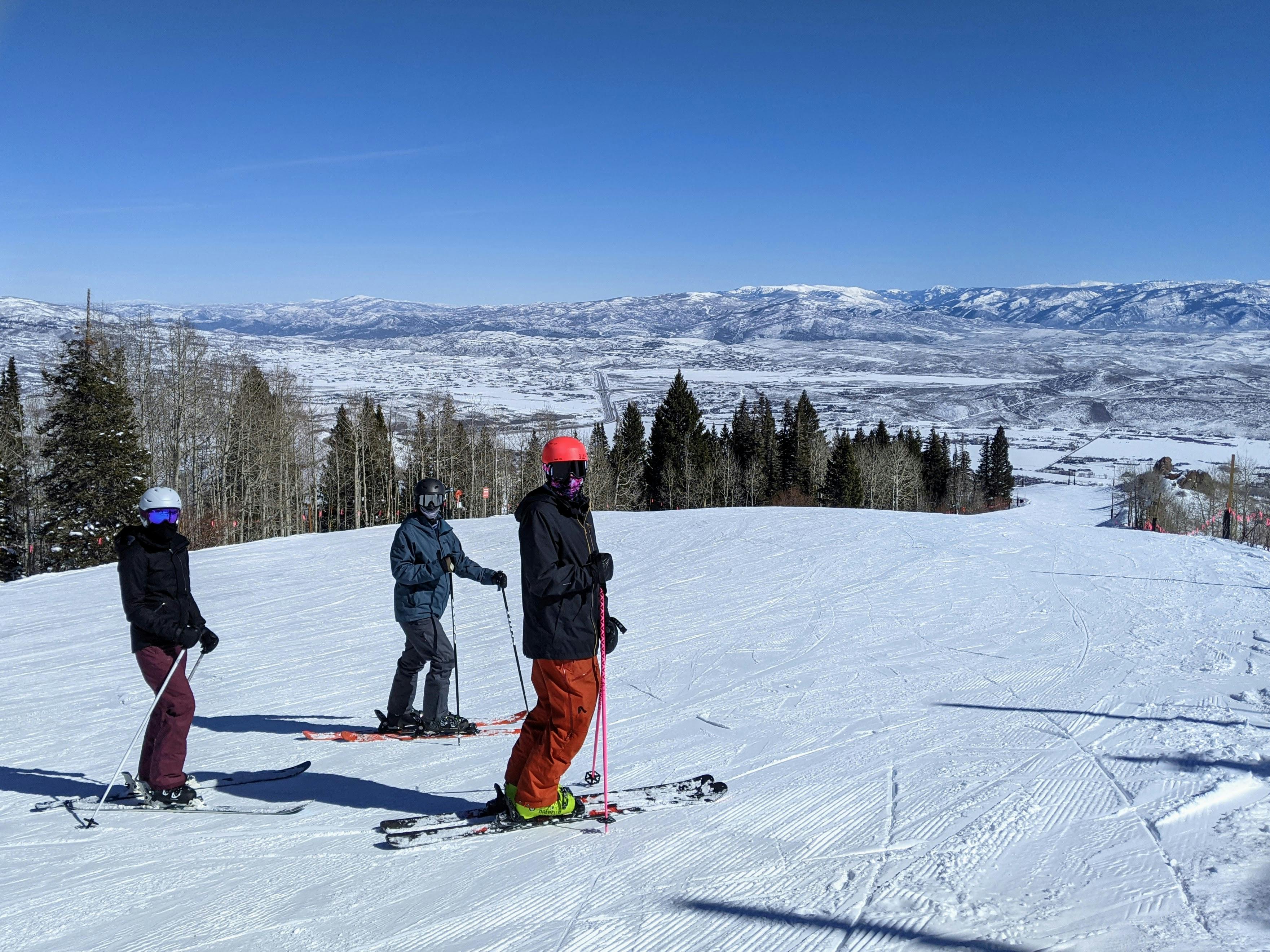 Three skiers standing on a ski run and smiling at the camera. 