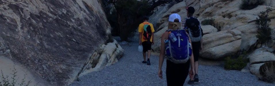 Three people walking towards a rocky wall. One is wearing the Osprey Talon 22 L backpack.